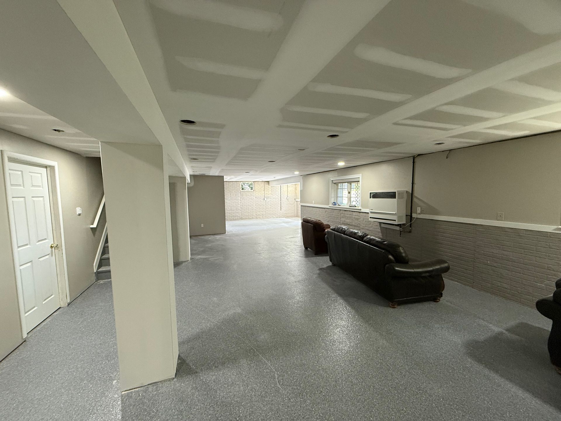 Empty basement with gray epoxy floor, columns, and a black leather couch.