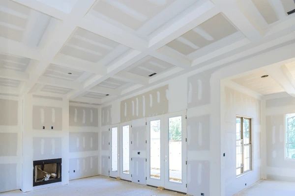 Room with newly installed drywall. Ceiling and walls are white, with a fireplace, windows and doors.