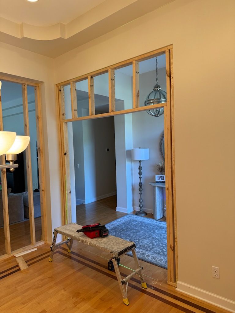 Mirror-lined hallway with a small bench and a view into a carpeted room with lamps and a window