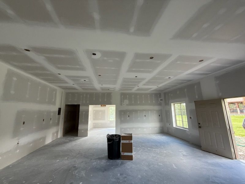 Interior of a room under construction with drywall on walls and ceiling; concrete floor.
