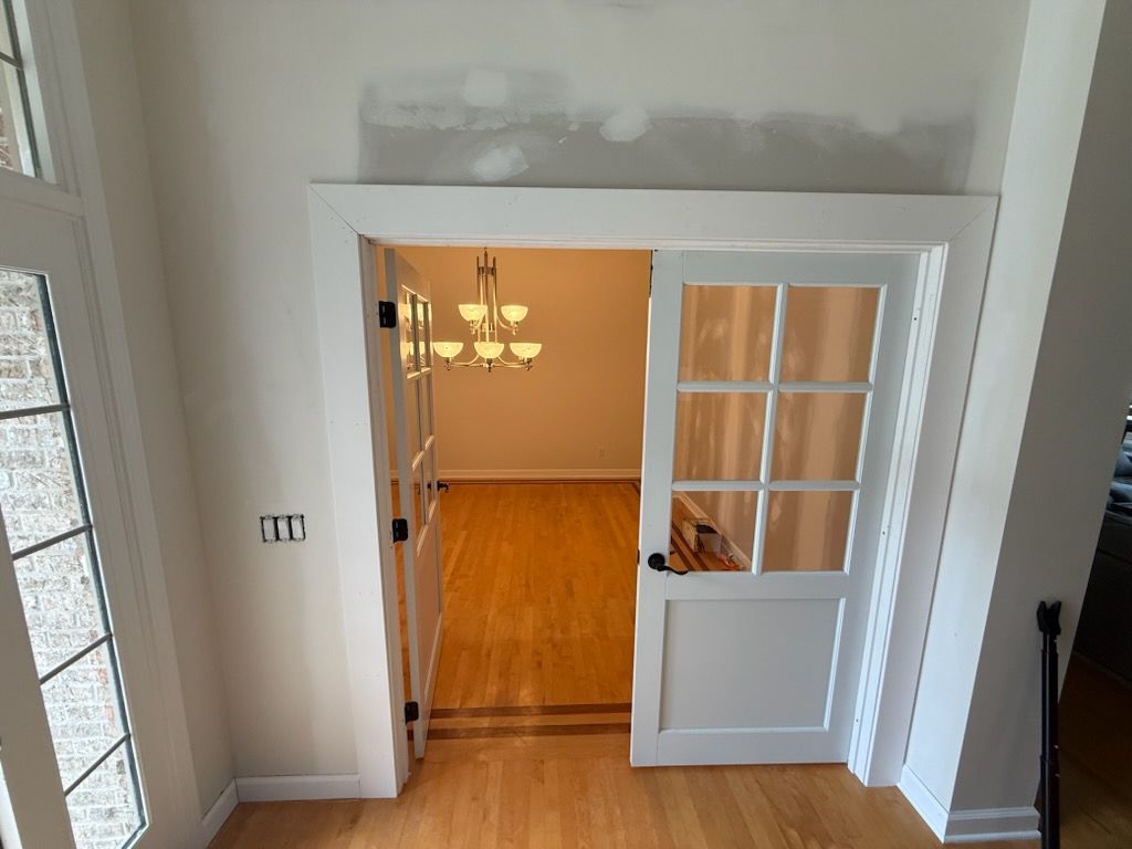 Stair landing overlooking an open doorway to a bright room with hardwood floors and a chandelier