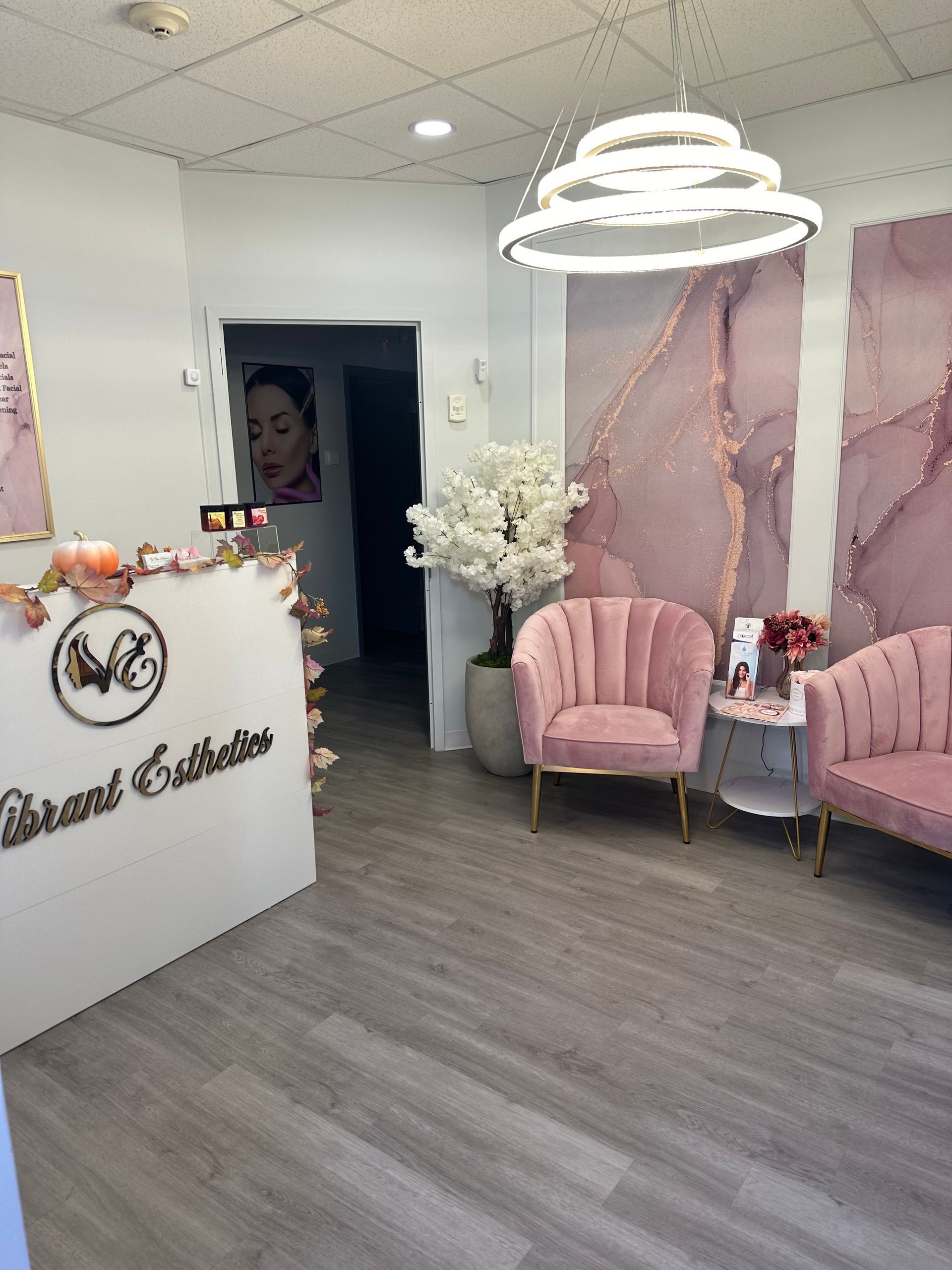 Reception area of Vibrant Esthetics salon with pink accents, seating, and a modern light fixture.