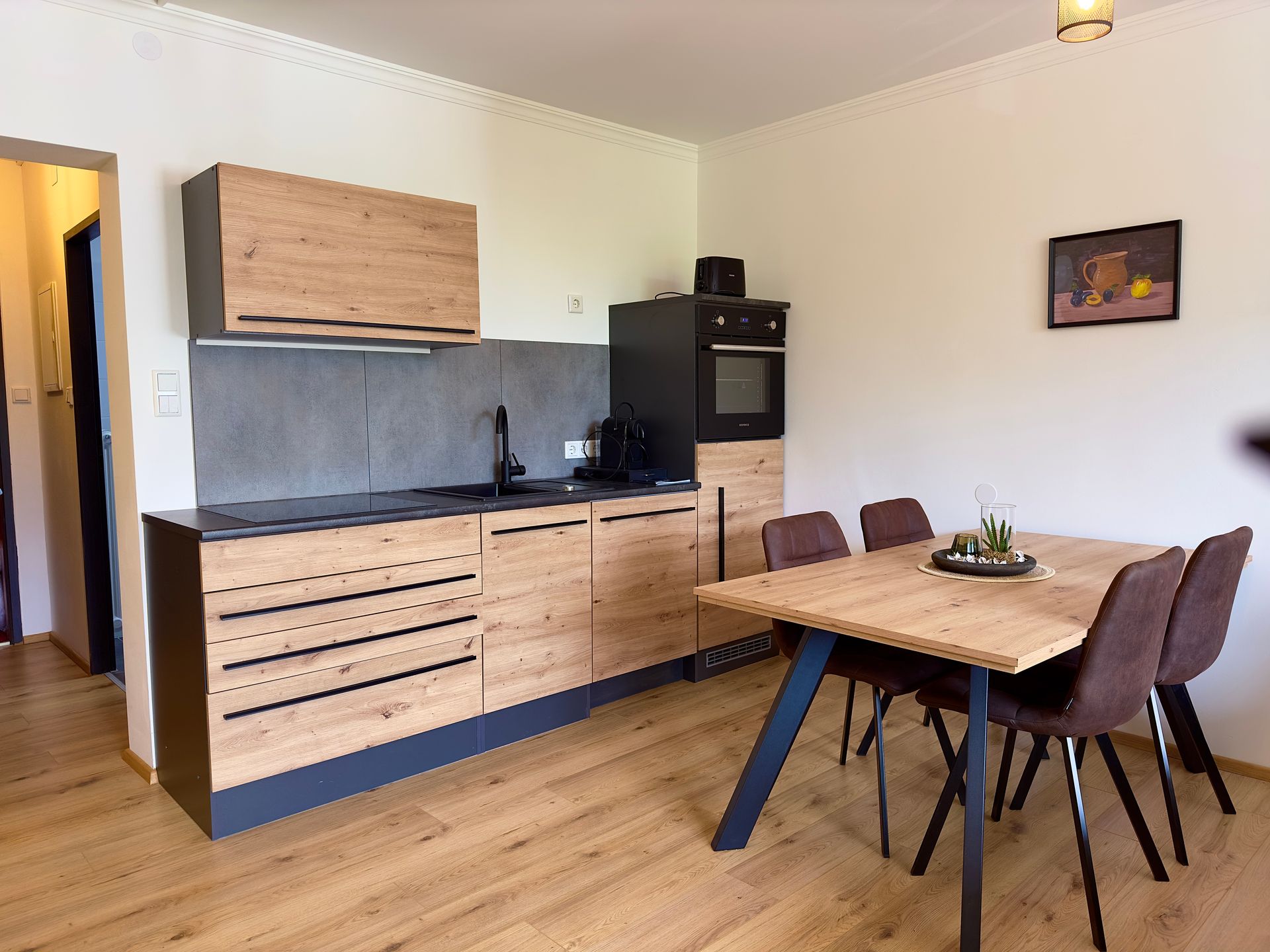 Moderne Wohnküche mit Holzschränken, schwarzen Elektrogeräten und einem Holztisch mit Stühlen