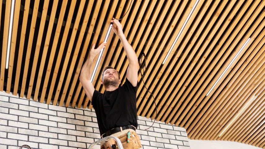 Person reaching up to install or adjust wooden ceiling slats in a bright interior room