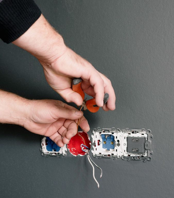 Hands wiring a red electrical component on a wall-mounted outlet box