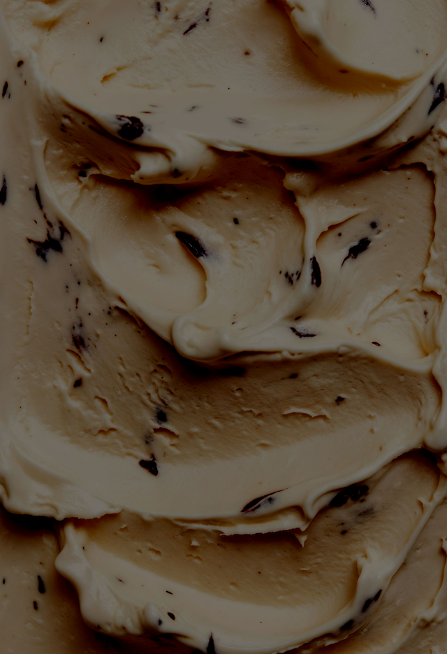 Primer plano de un helado de color beige y marrón con remolinos y motas de chocolate.