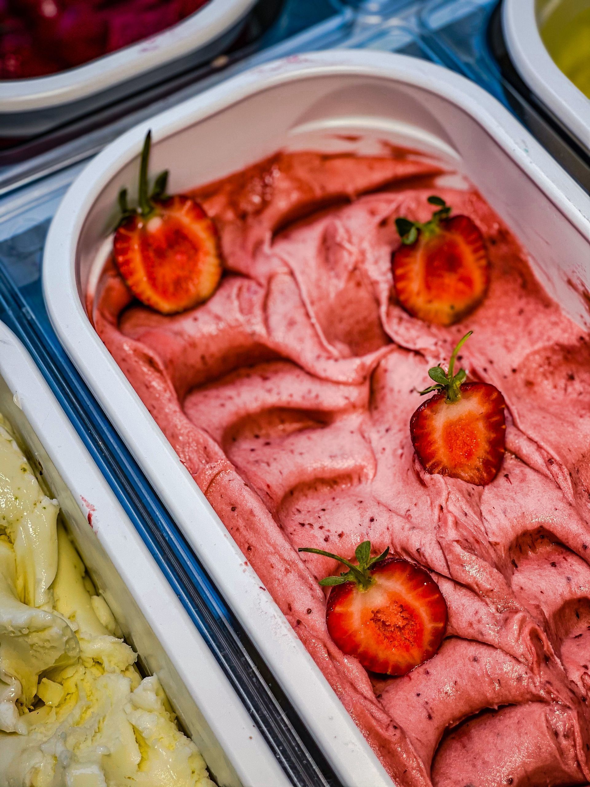 Helado de fresa rosa cubierto con fresas cortadas por la mitad en una bandeja de metal.
