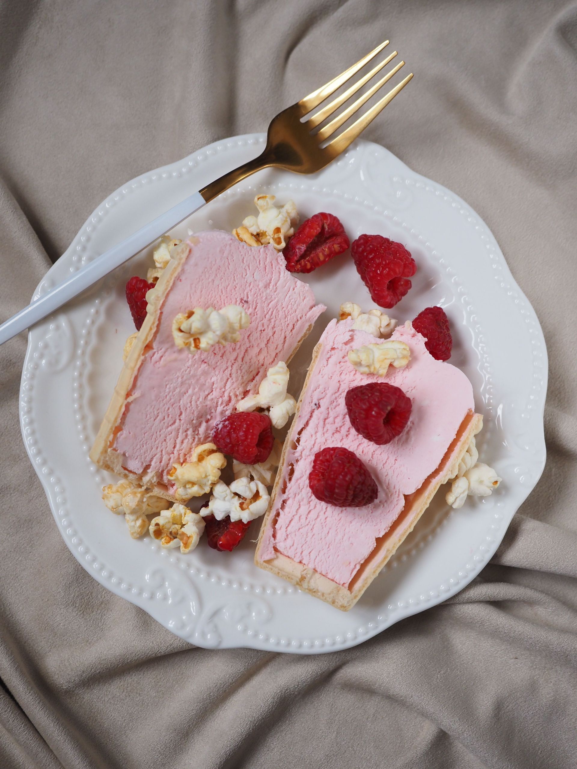 Rebanadas de pastel rosa en un plato blanco con frambuesas y un tenedor dorado.