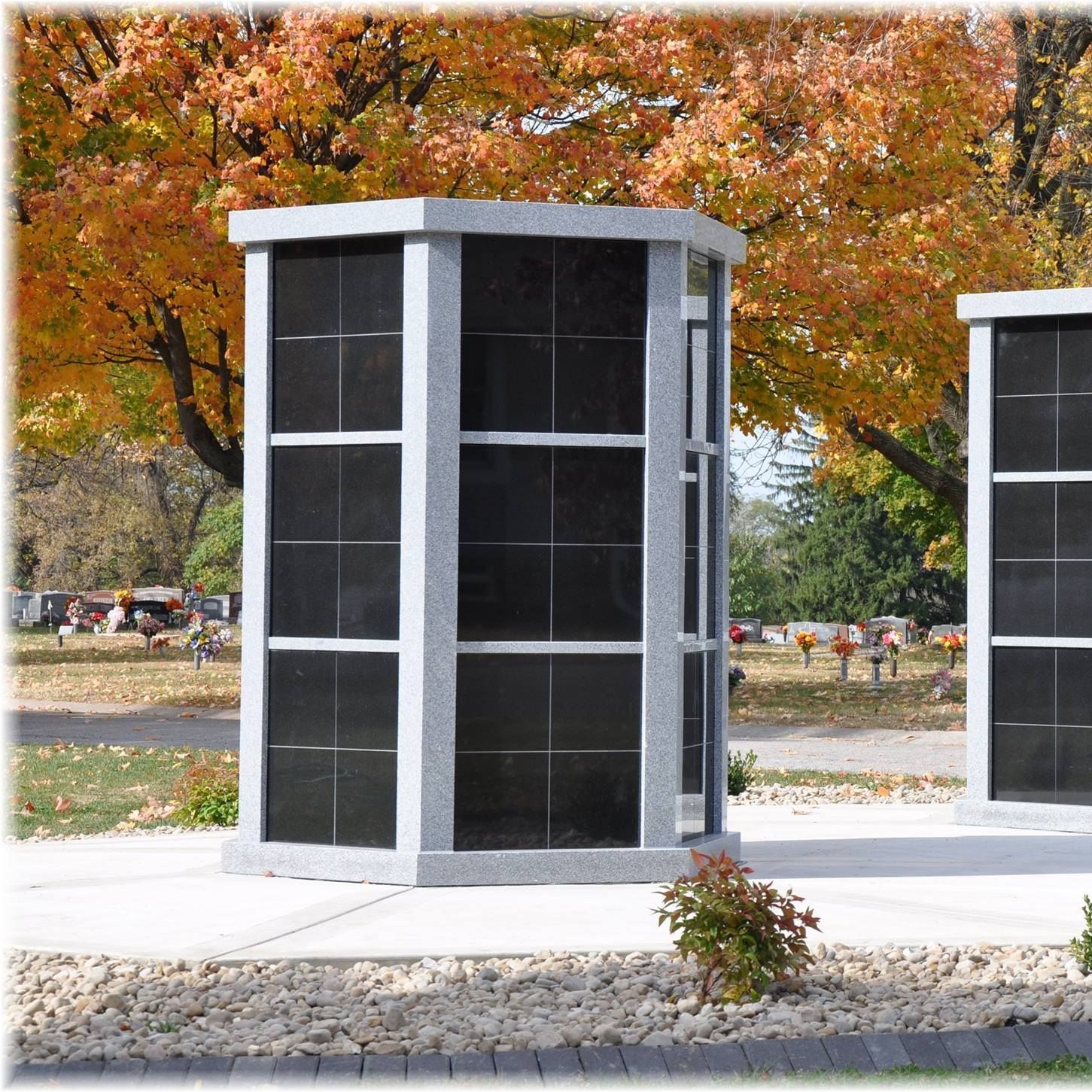 Outdoor mausoleum with multiple black niches, set in a cemetery with autumn foliage.