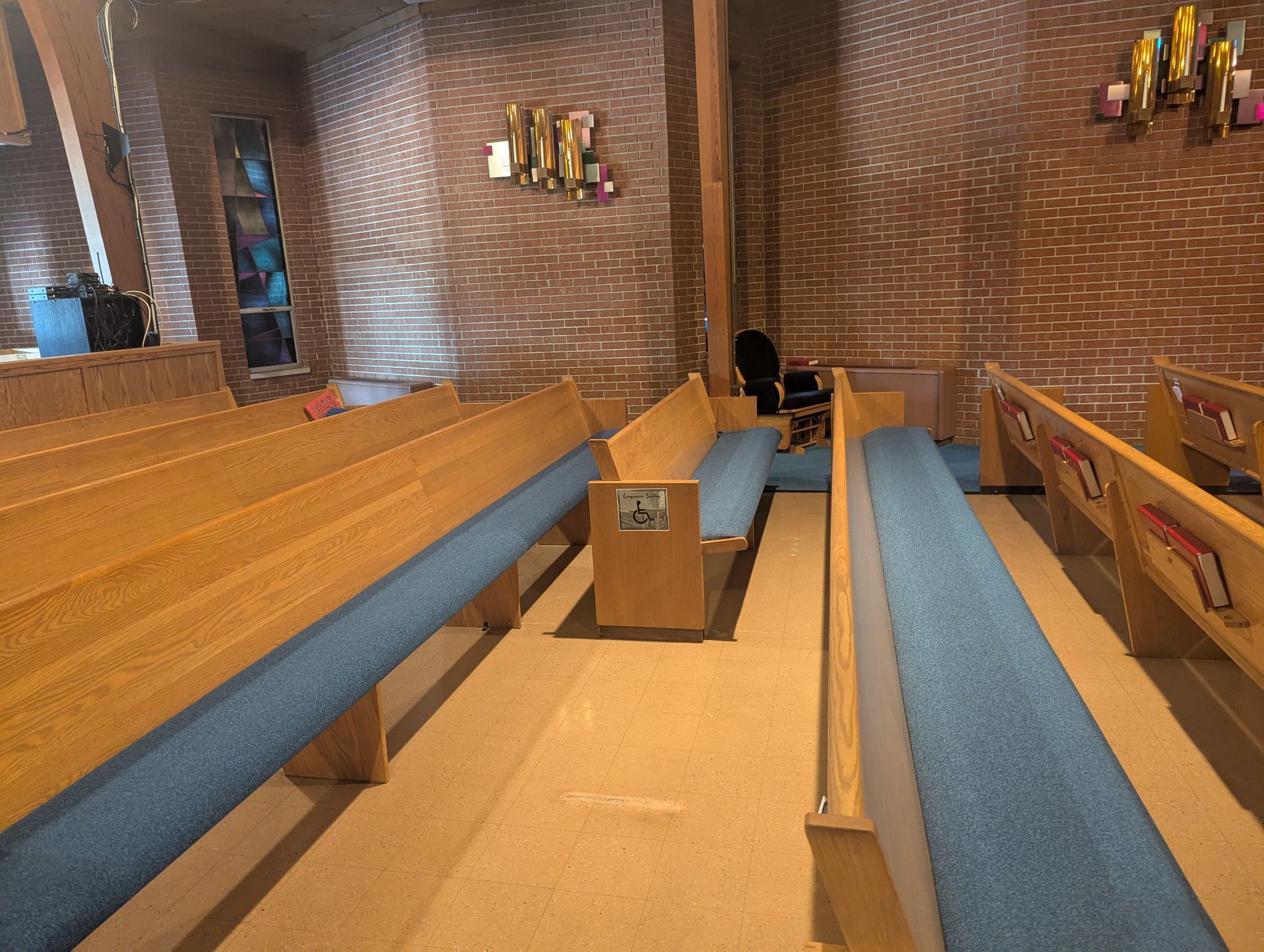 Empty church pews with blue cushions in a brick-walled sanctuary