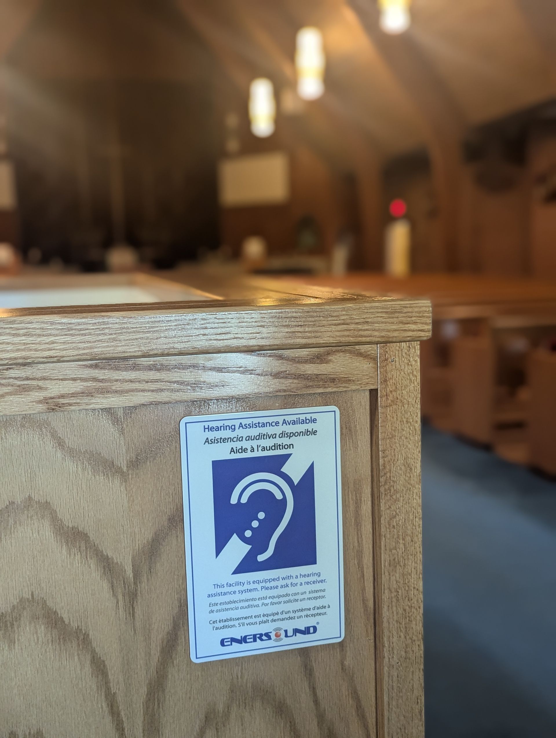 Blue hearing assistance sign on a wooden pew in a church interior.