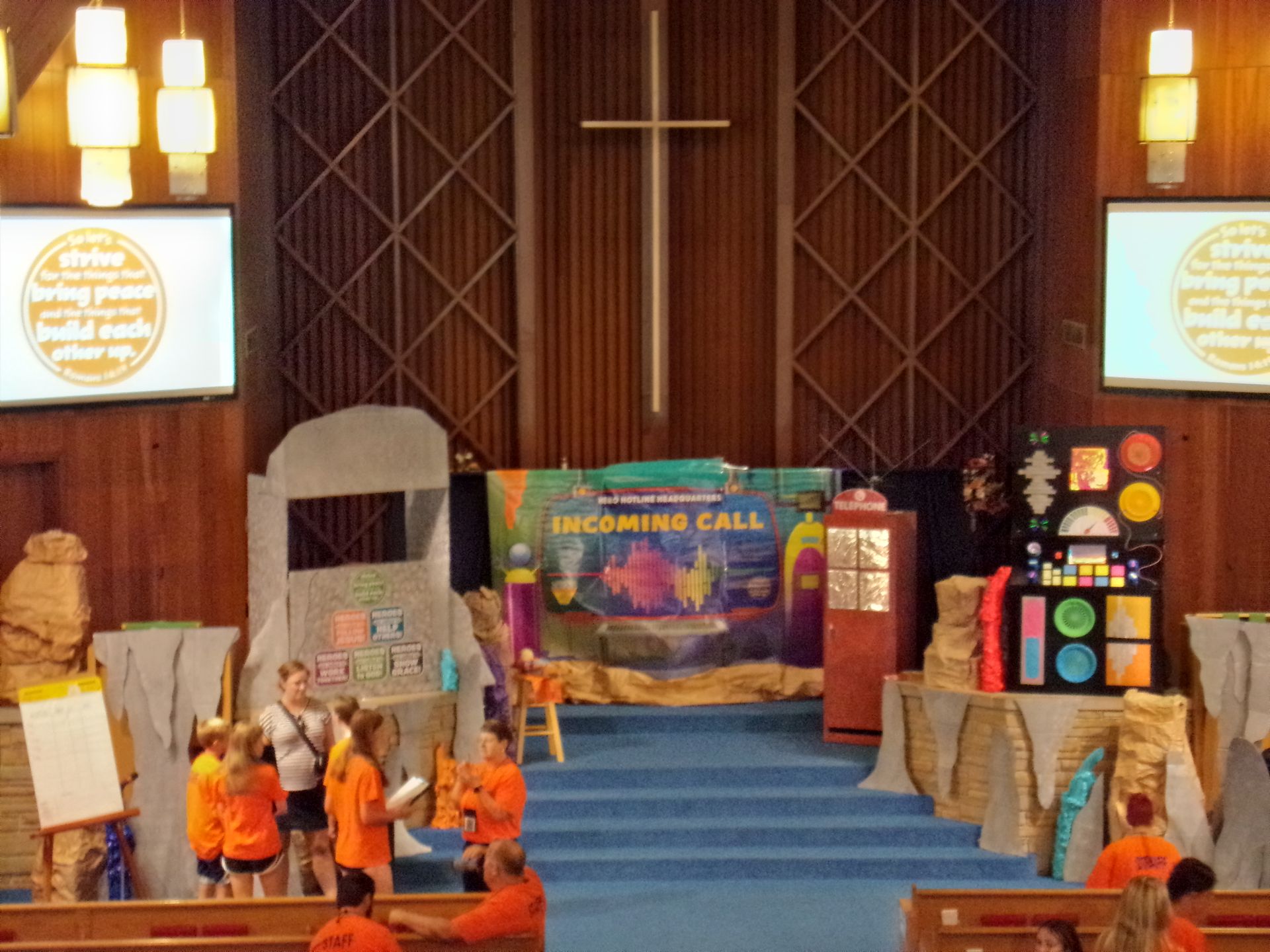 Church stage with children in orange shirts performing beneath a cross and colorful backdrop