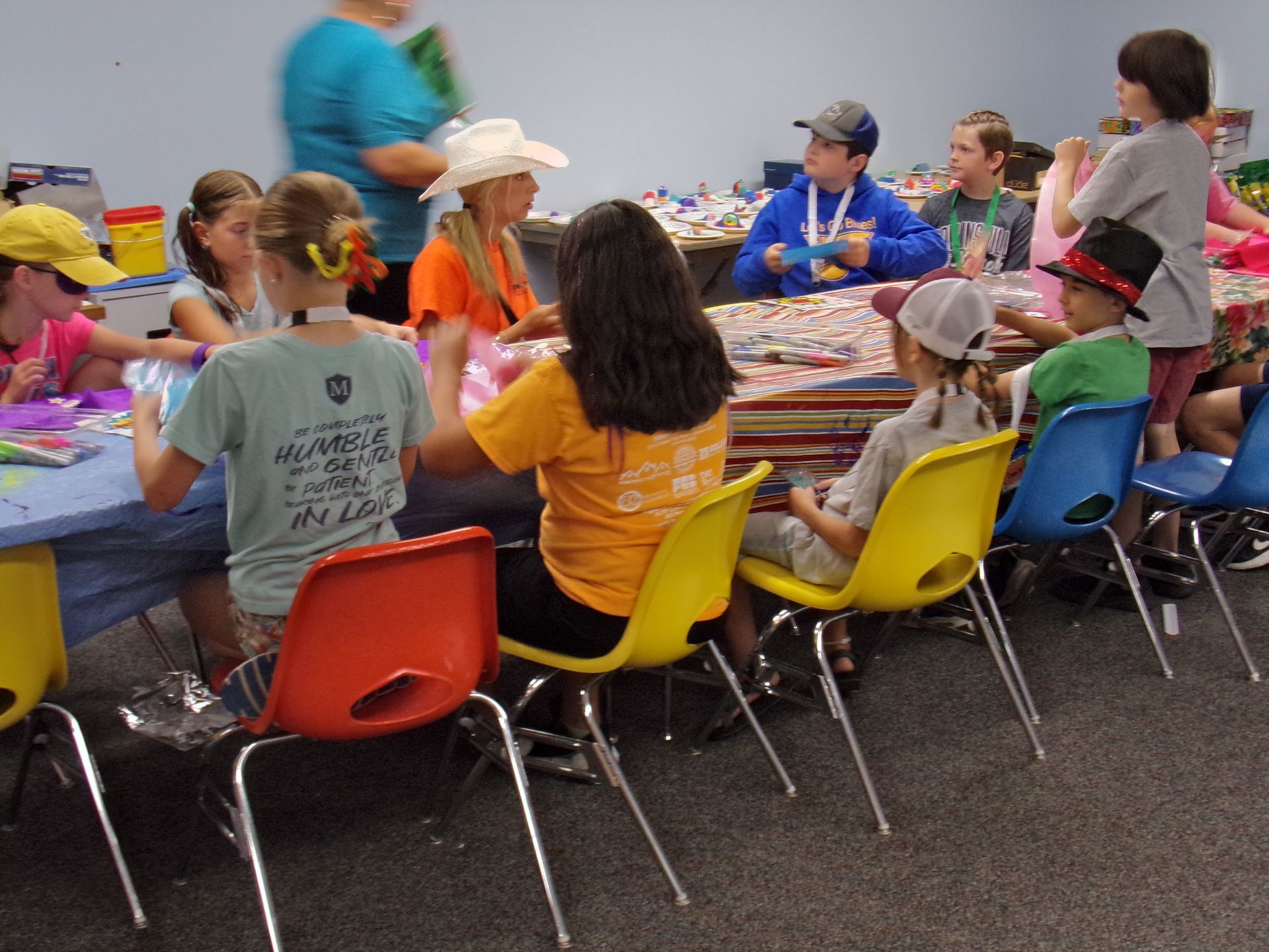 Children seated at a long table, painting and crafting in a colorful classroom activity.