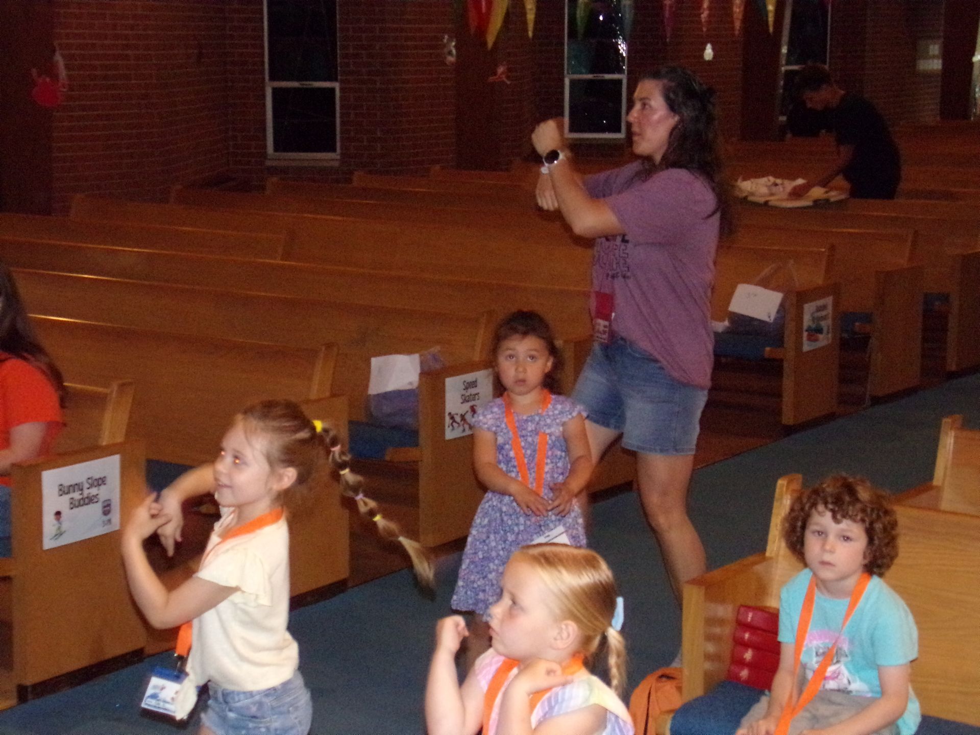 Children on pews and a woman taking a photo in a church-like hall