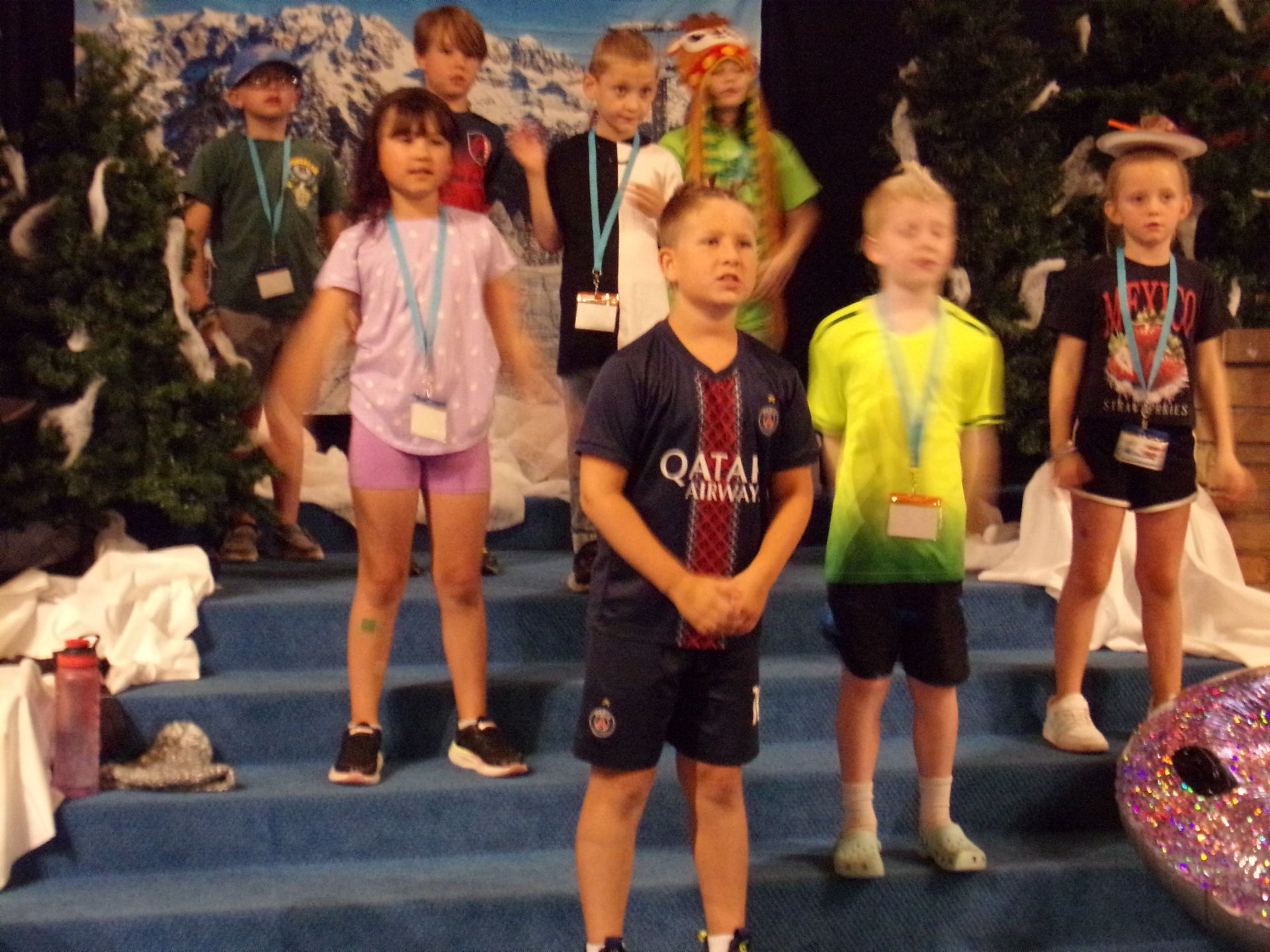 Children in sports outfits standing on a blue podium with medals at an indoor event