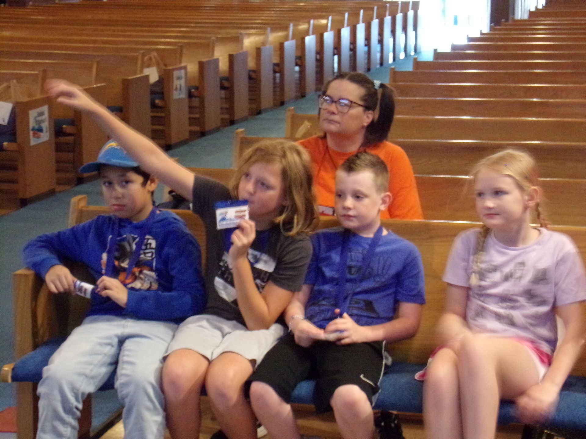 Children sitting on pews in a church, one pointing left while an adult sits behind them