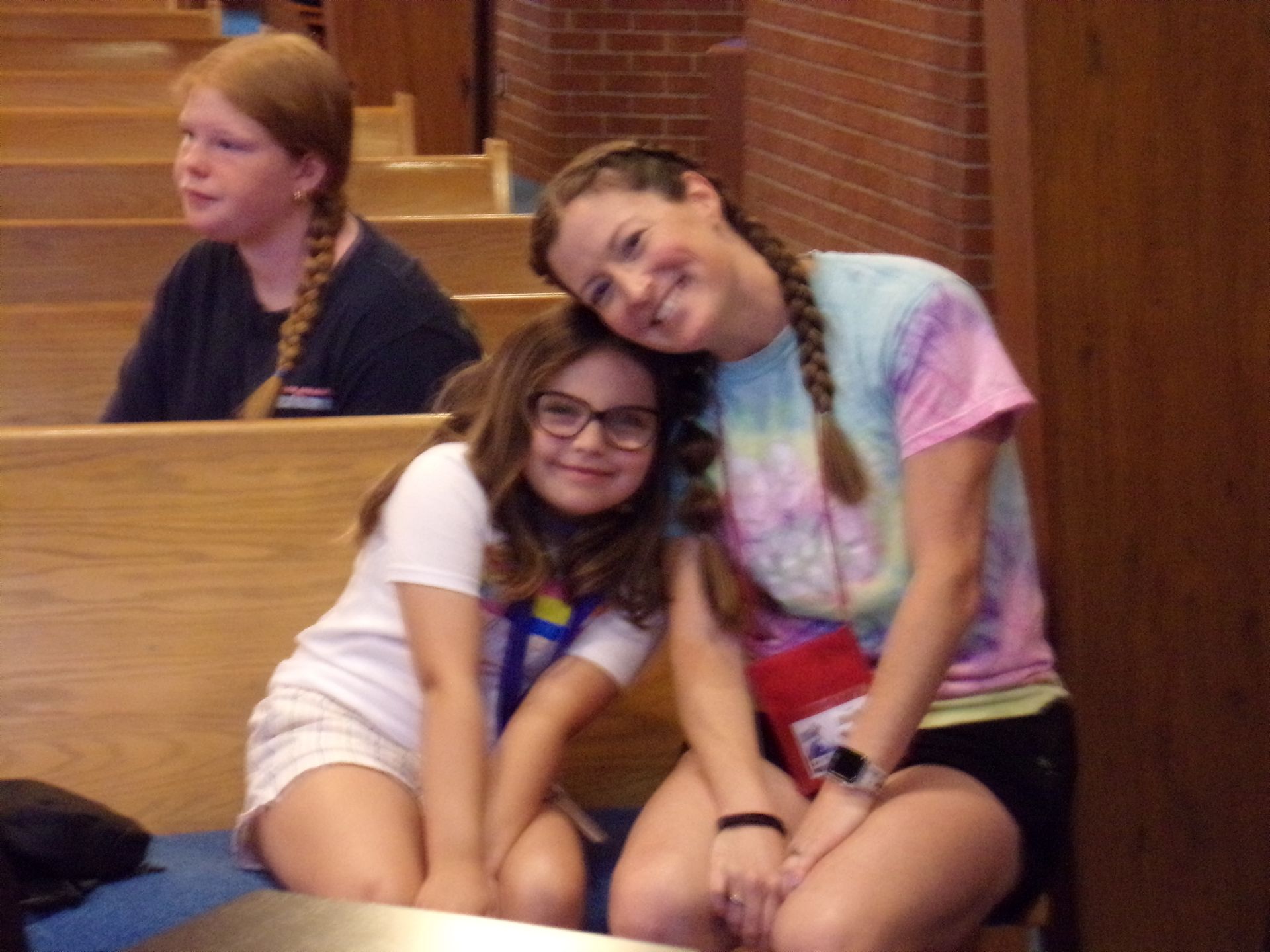 Two girls sitting together on a bench, smiling, with one resting her head on the other's shoulder.
