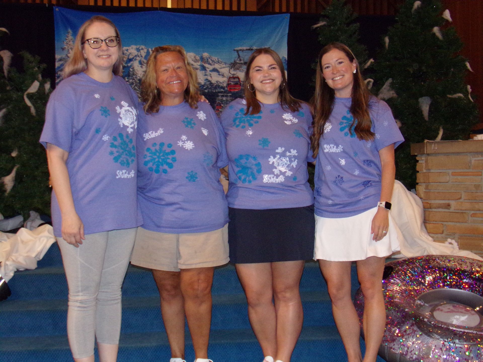 Four people in matching purple shirts pose outdoors in front of a festive holiday display.