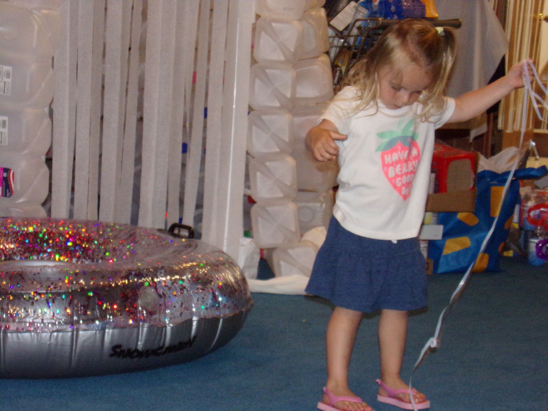 Child holding a string stands in a playroom beside an inflatable toy