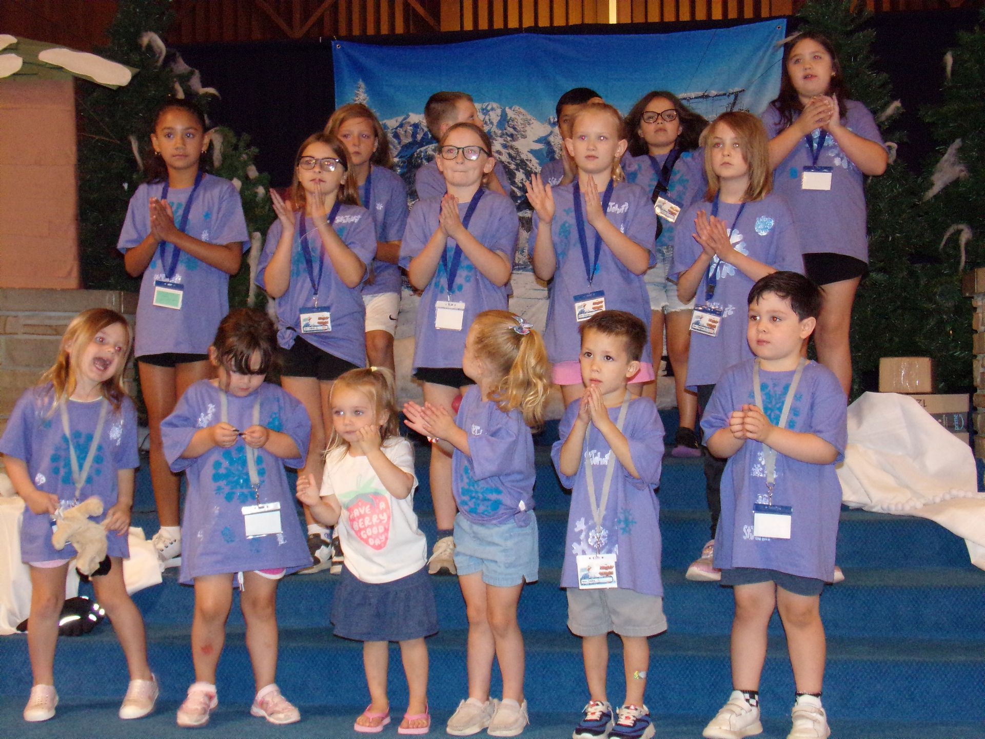 Children in purple shirts on a stage, holding medals and clapping during a group celebration