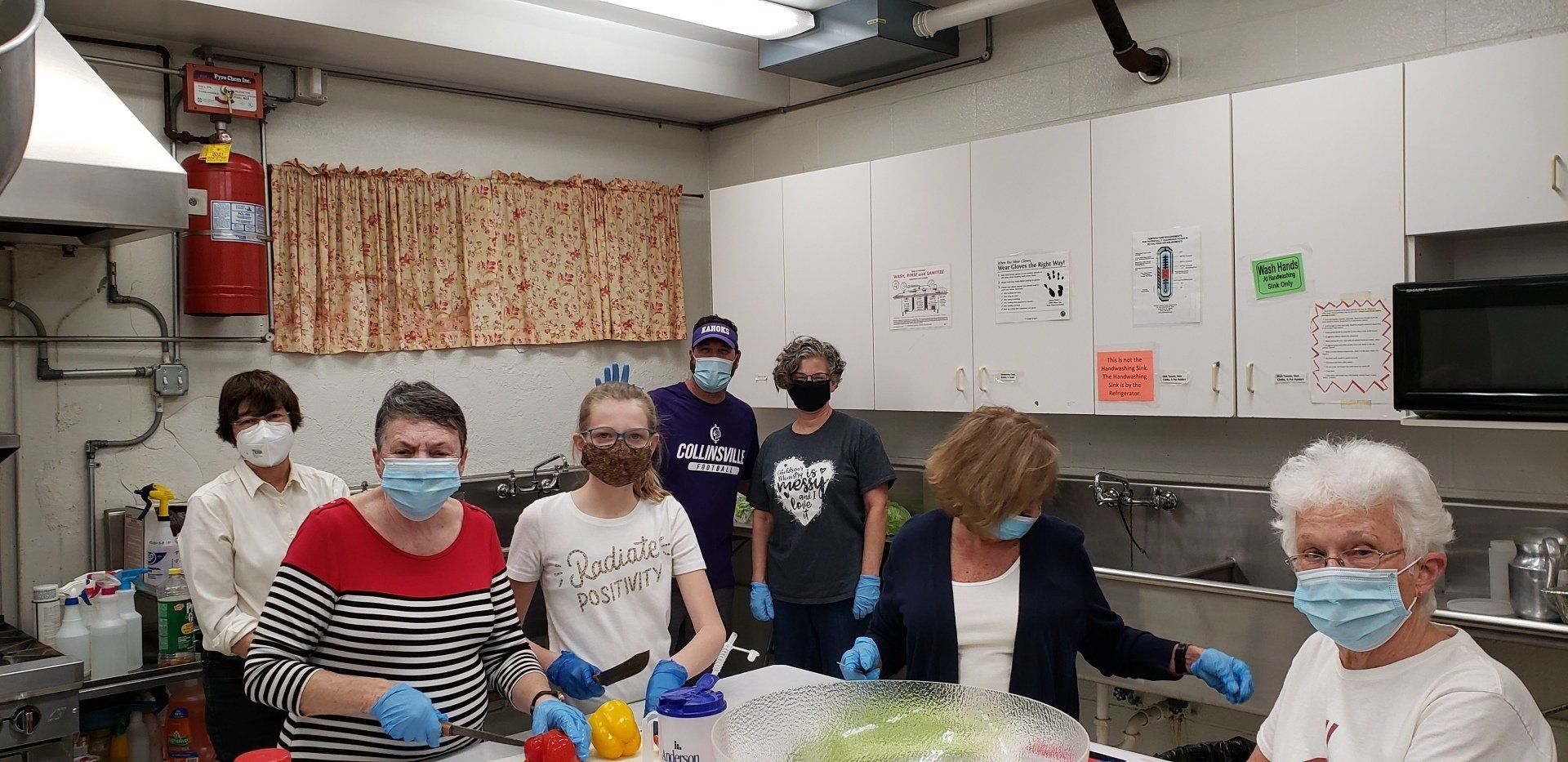 Masked people sitting around a table in a kitchen, preparing food and talking