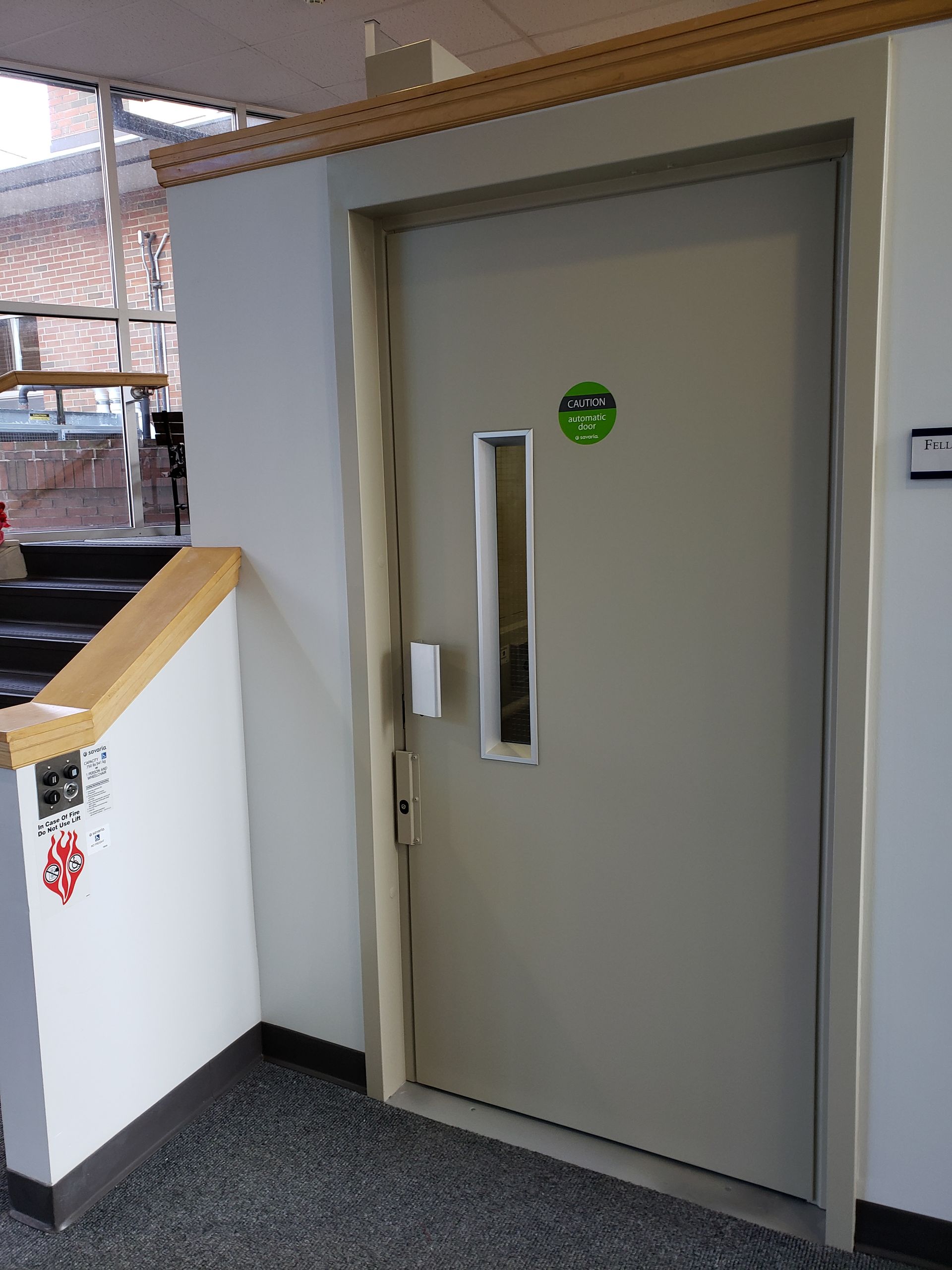 Office hallway with a gray door, narrow window, and green sign above the handle