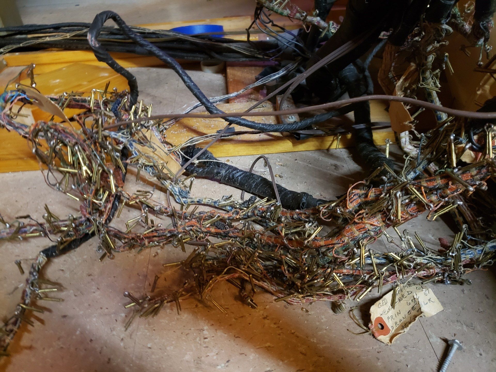 Tangled exposed electrical wires and cables spread across a floor near a power strip and tools