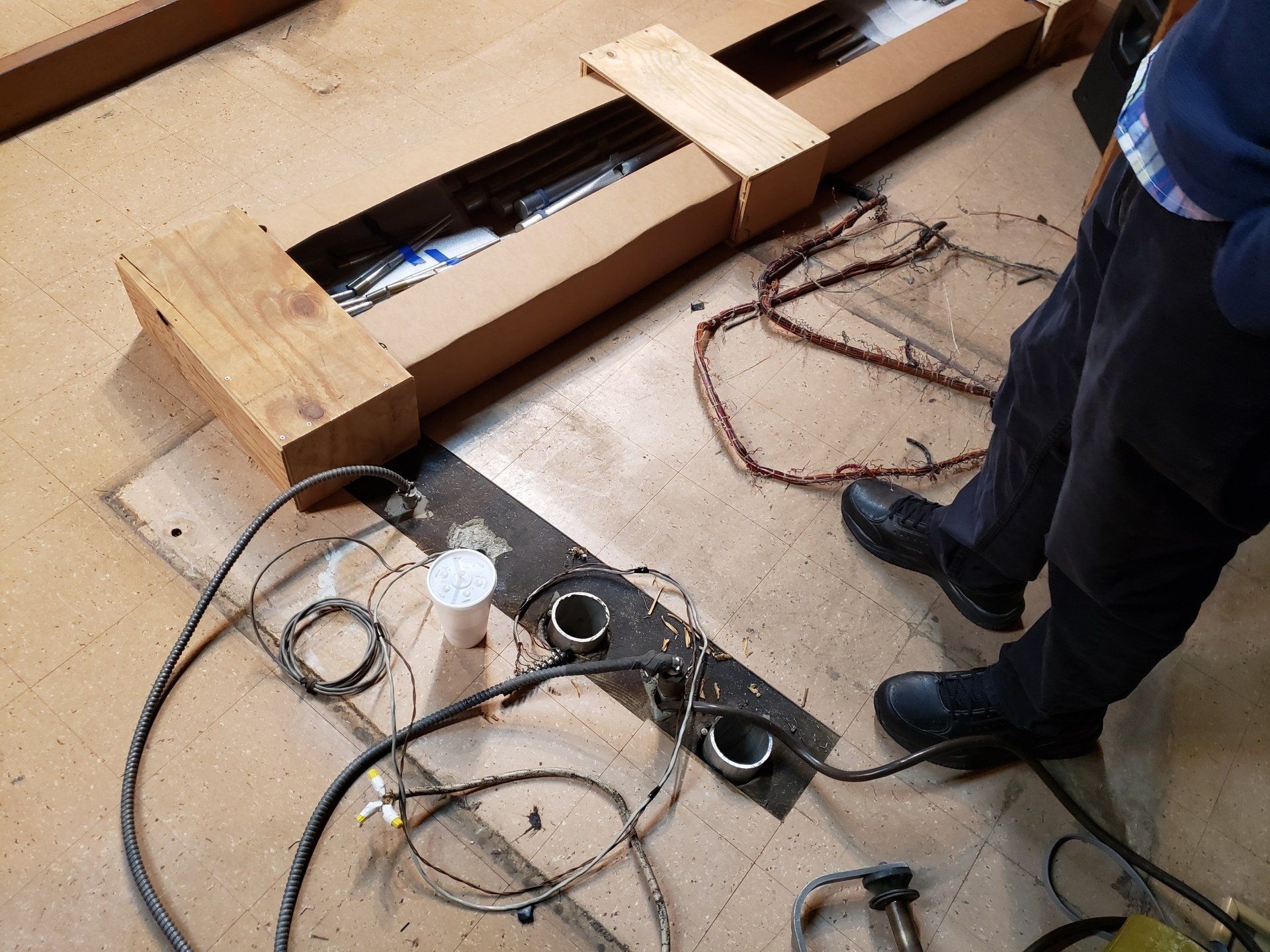 Worker stands beside a cardboard-covered floor with cables and large wooden boards.