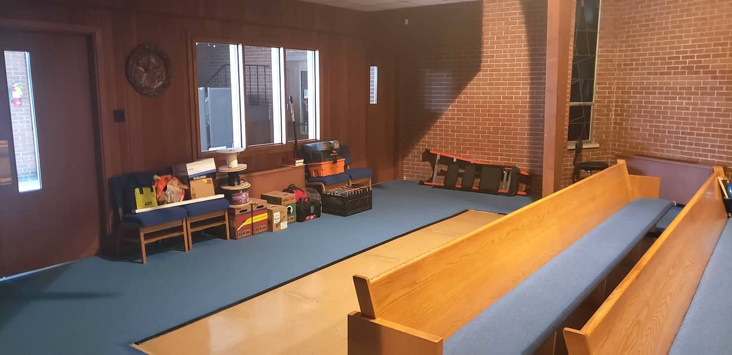 Empty room with blue carpet, wooden pews, and chairs by windows in warm light