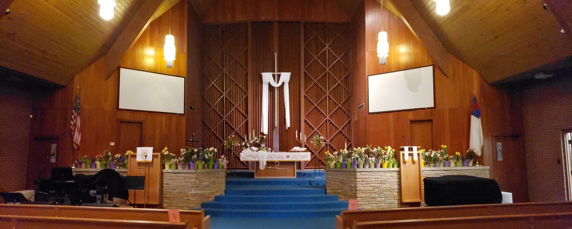 Church sanctuary with blue-carpeted steps, altar, and wood-paneled walls under warm lighting