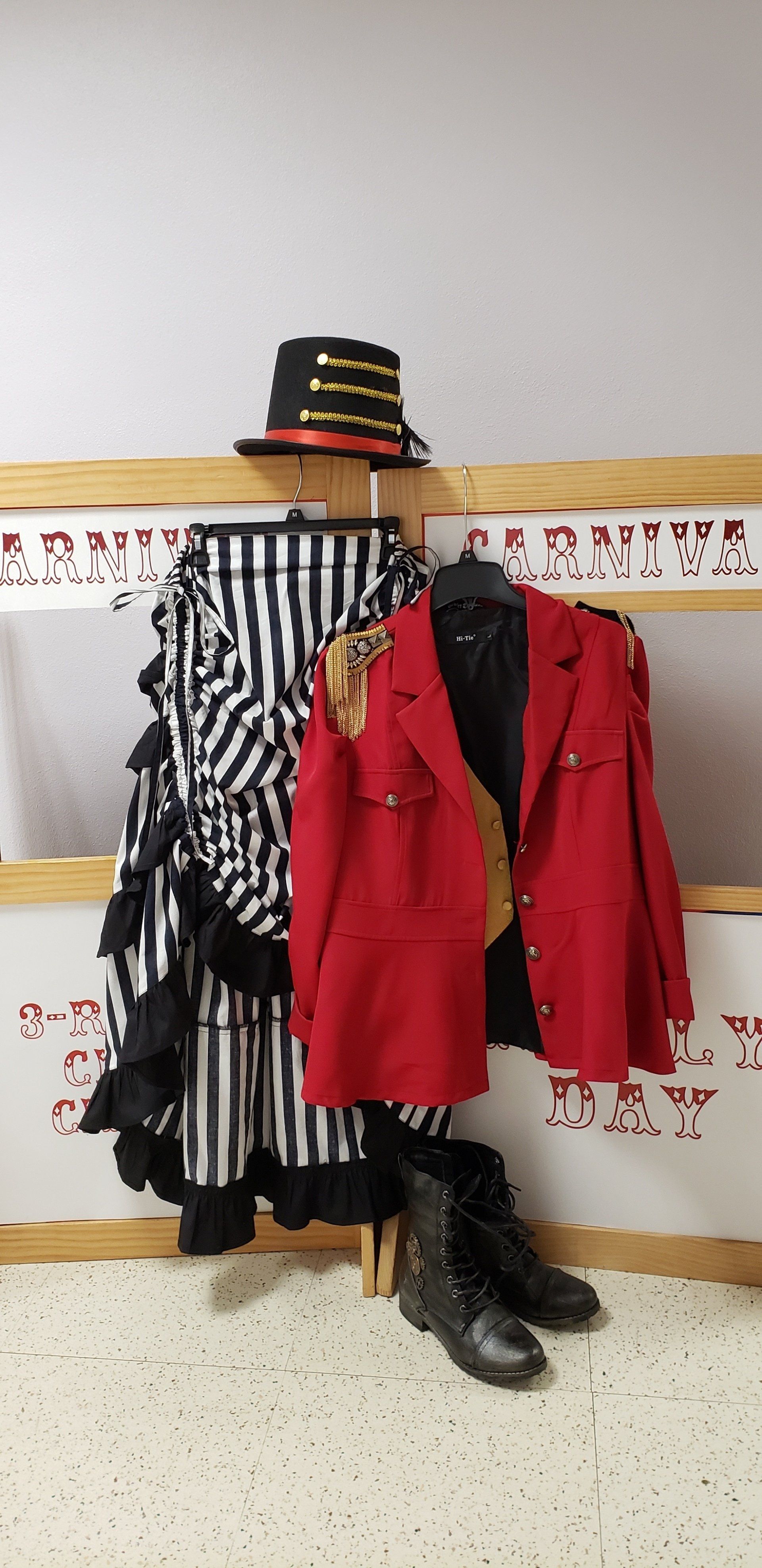 Two mannequin outfits: red jacket with black-and-white striped coat, black hat, and boots against a classroom wall