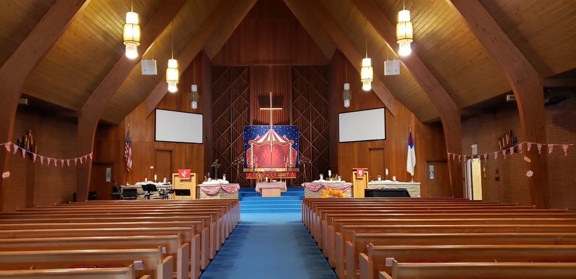 Wood-paneled church sanctuary with pews, hanging lights, and a blue-lit altar at the far end