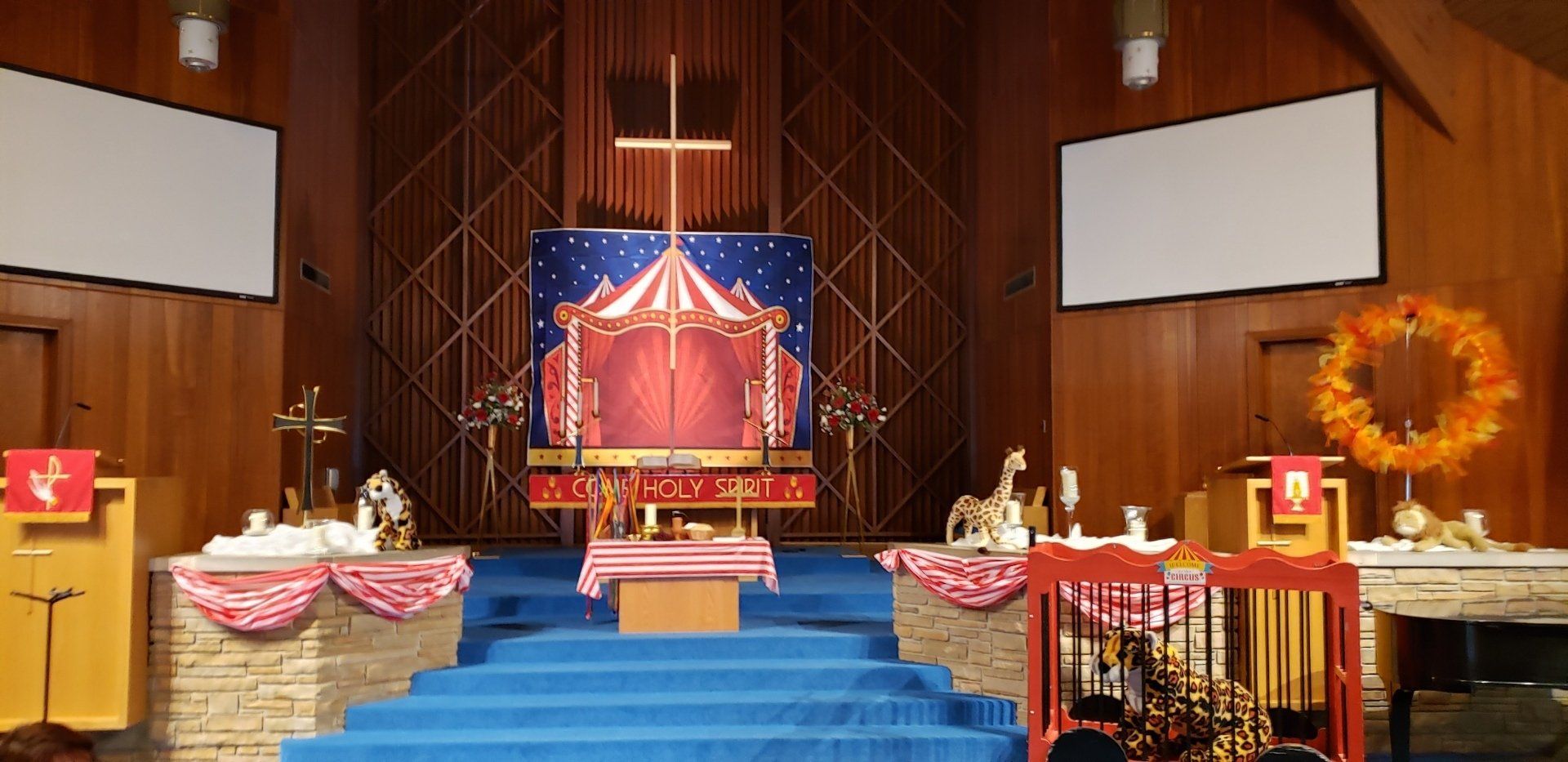 Church altar with blue steps, red-and-gold decor, and a lit central tapestry under wood-paneled walls