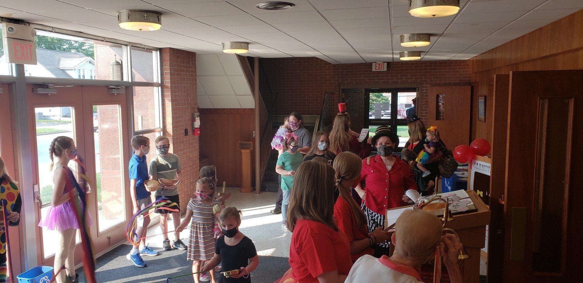 People gathered in a bright lobby near glass doors, some standing and some sitting at tables.