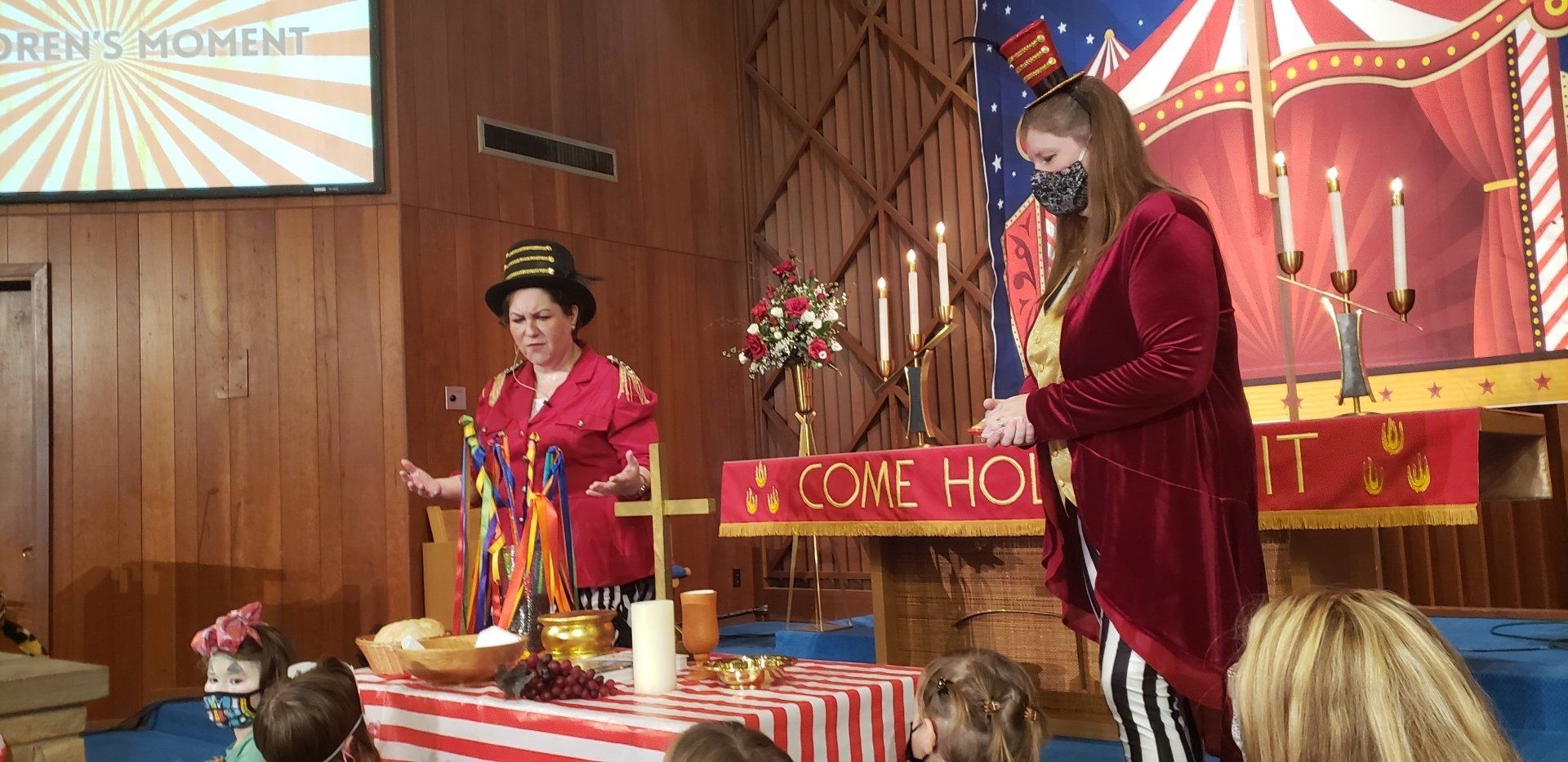 Two people in festive red costumes on a decorated stage with candles and a “Welcome home” sign