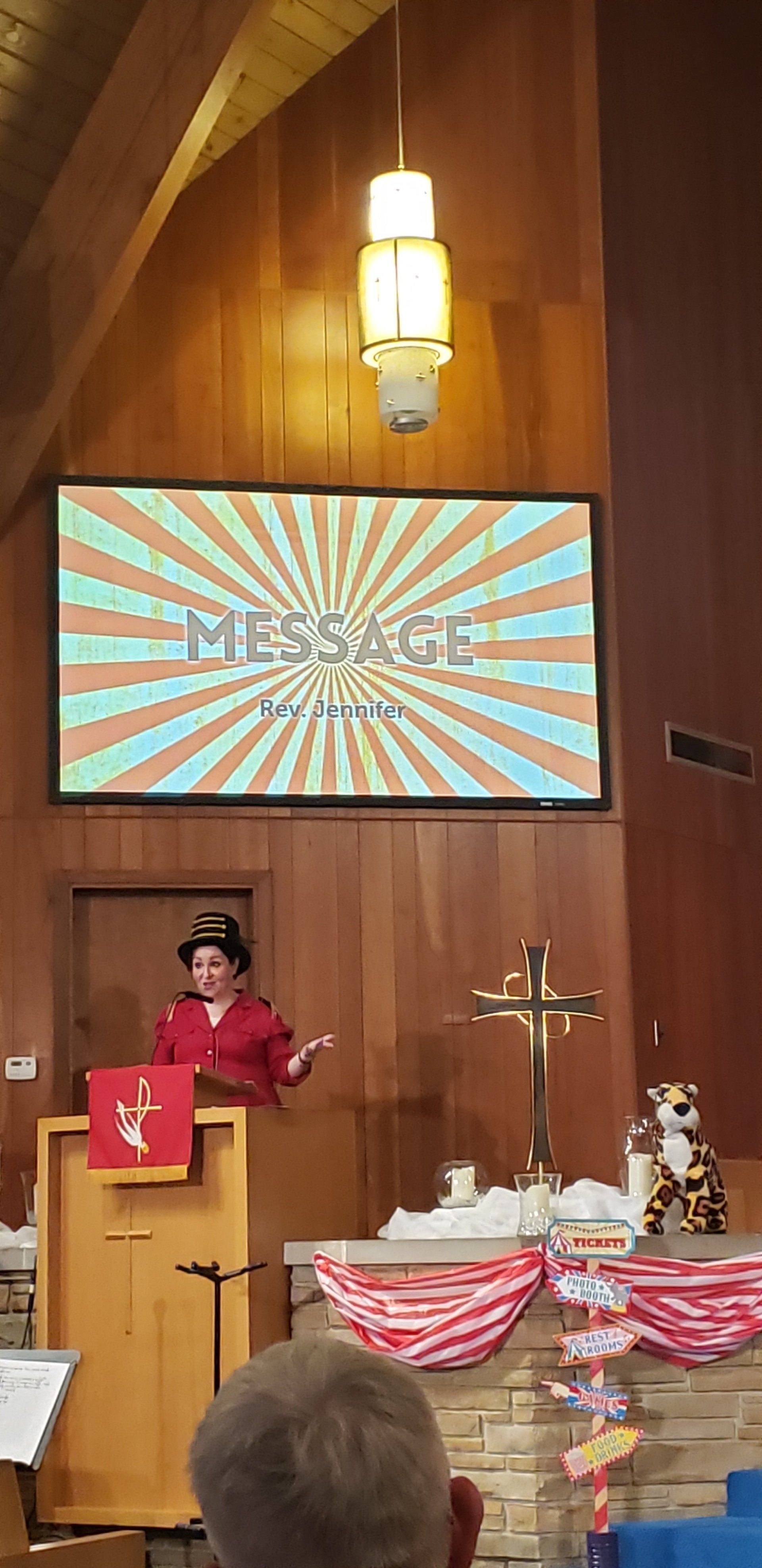 Speaker at a church podium with a “MESSAGE” slide projected behind, cross and candles nearby