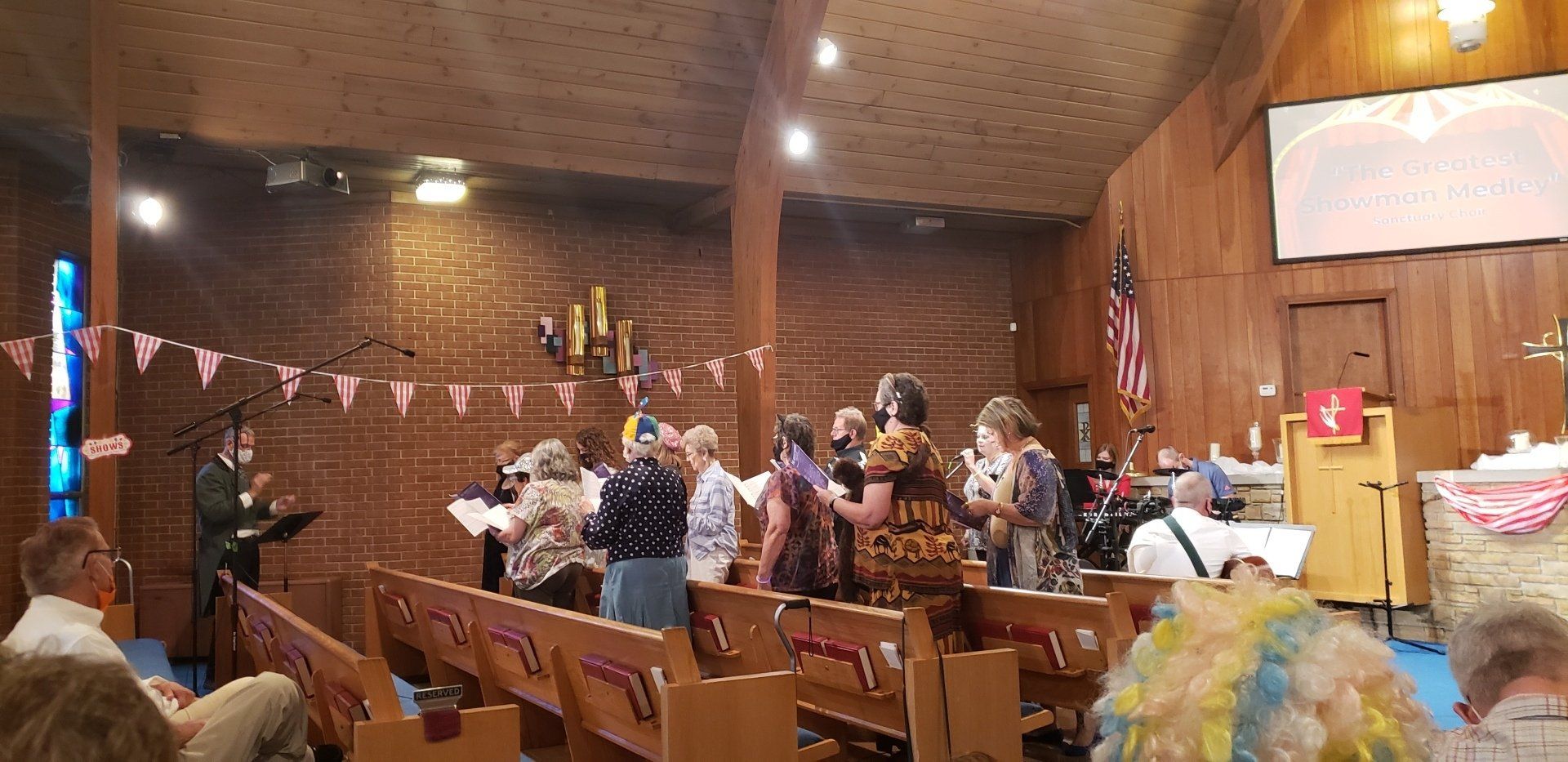 Congregation gathered in a wood-paneled church, many standing and clapping near the altar during a service