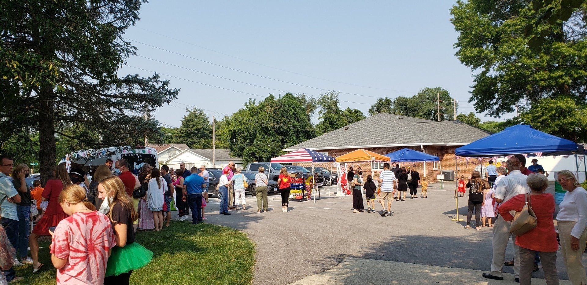 Outdoor community fair with people, vendor tents, and colorful umbrellas on a sunny day