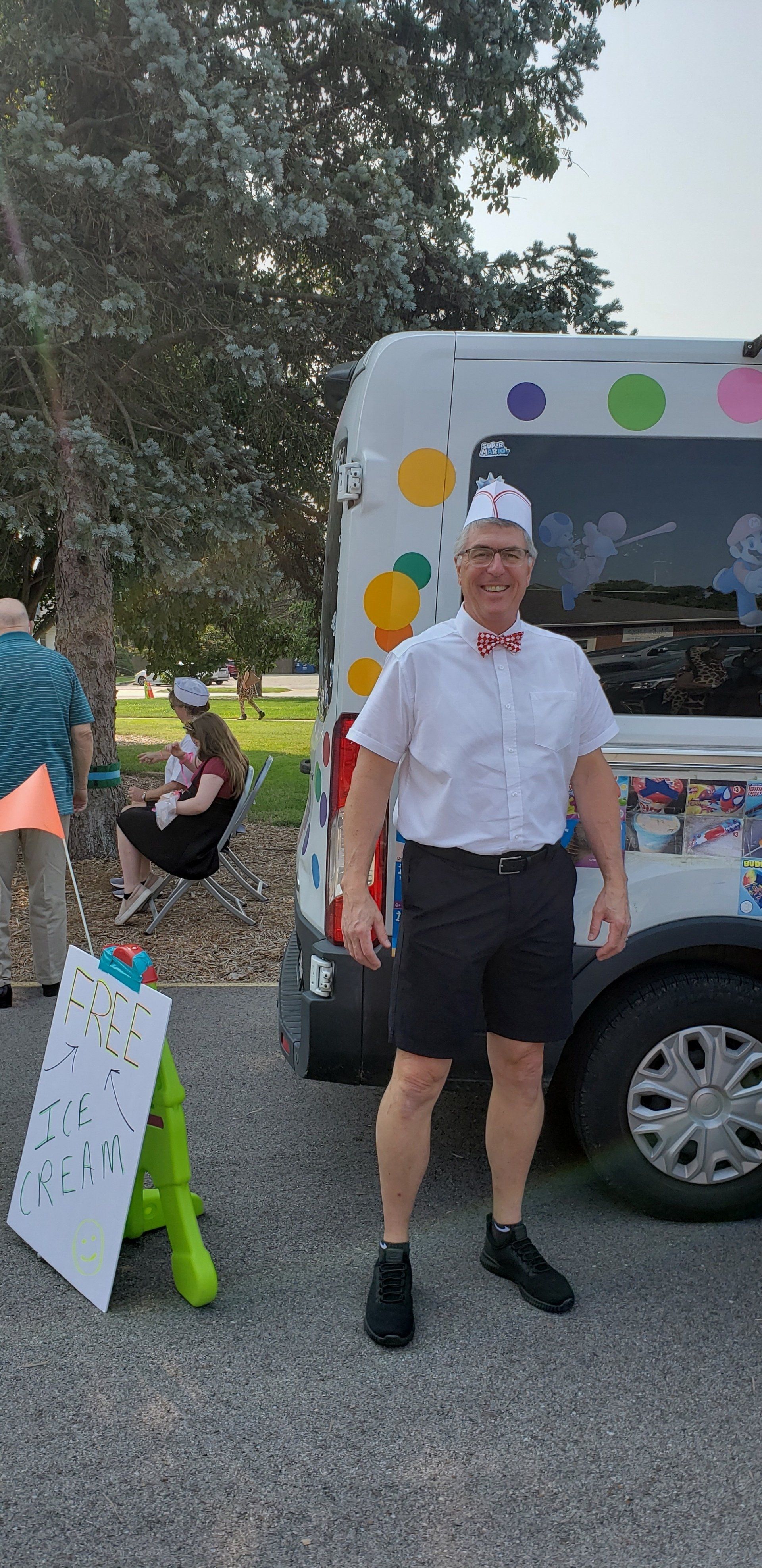 Man standing beside a decorated van at an outdoor event, with another person and a sign in the background.