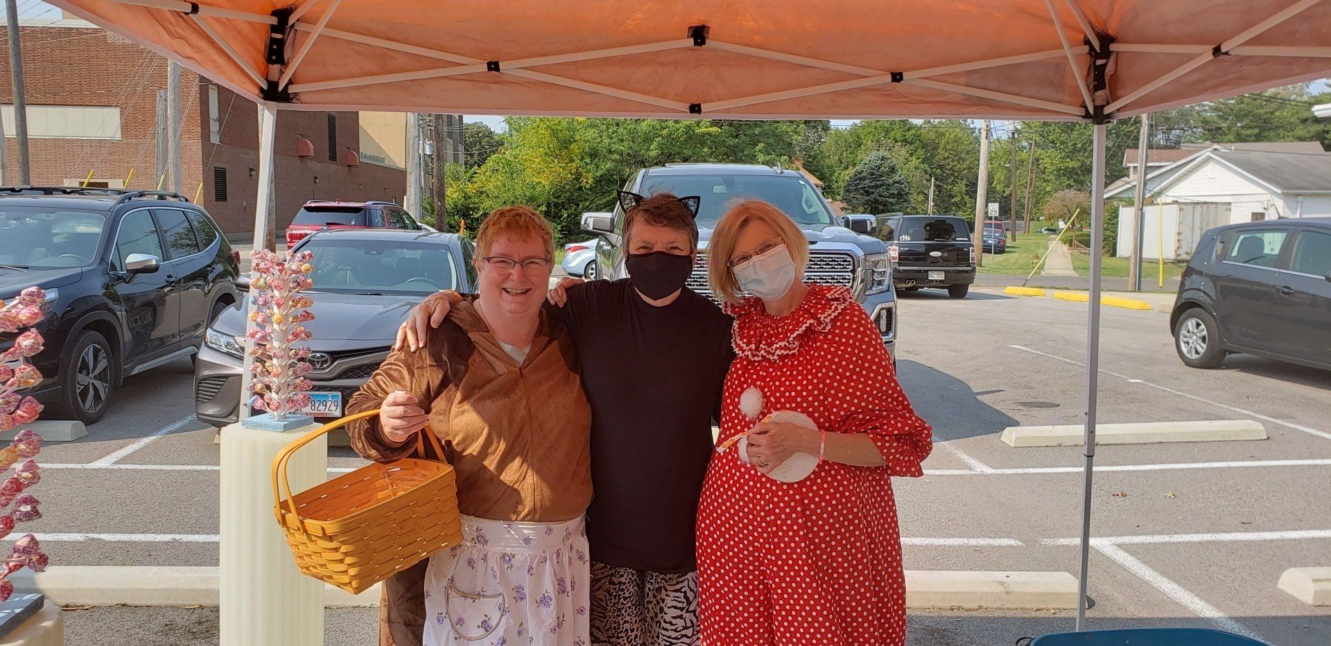 Three people posing under an orange canopy, one holding a basket and two wearing face masks.