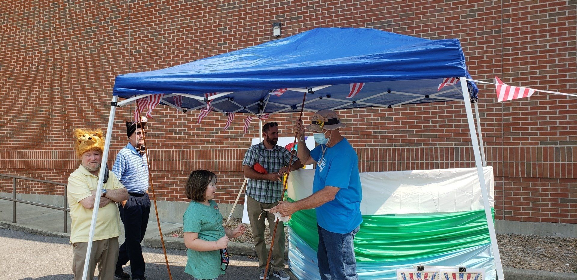 People gathered under a blue canopy tent with a table, serving food or drinks outdoors.
