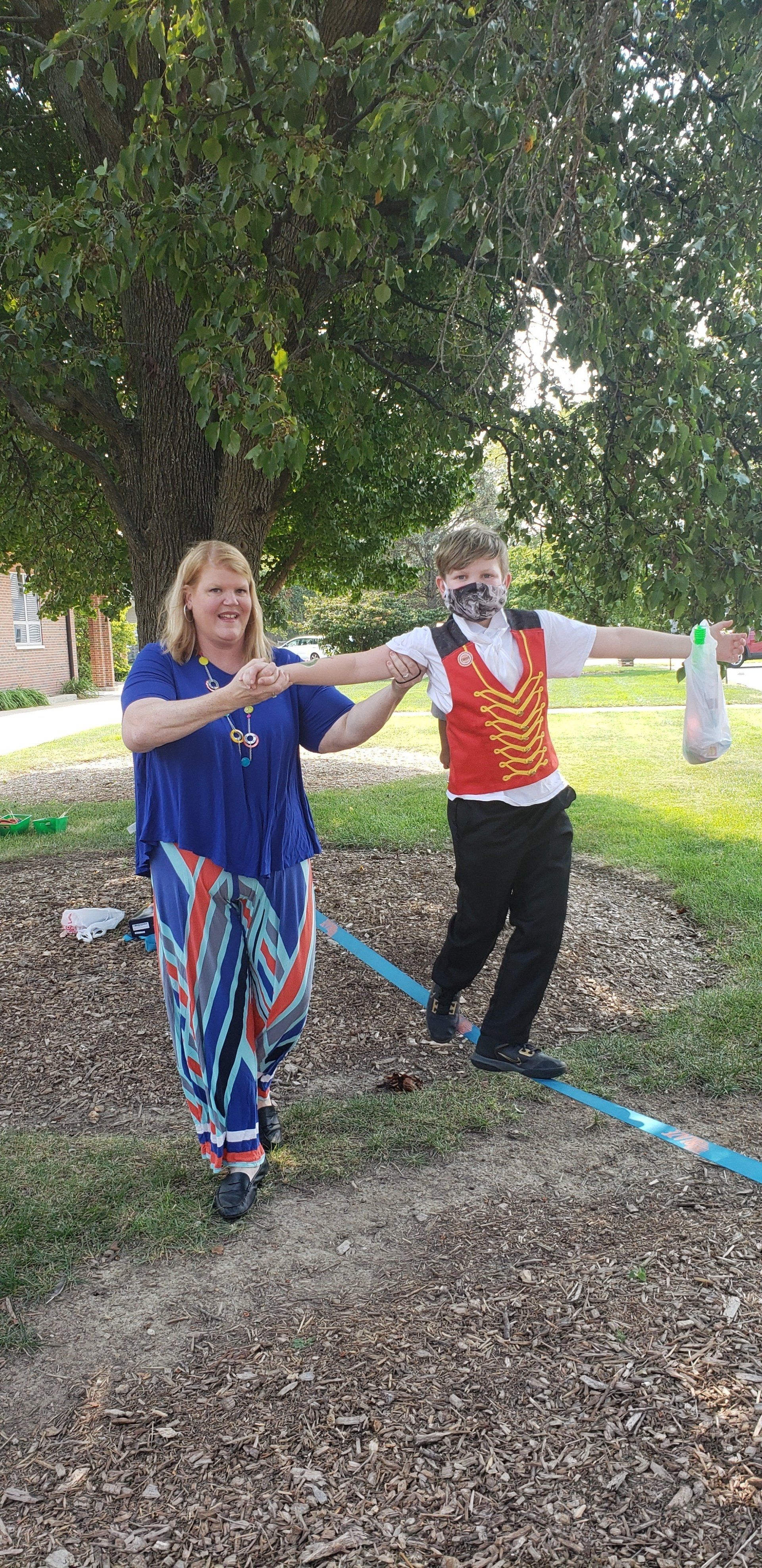 Two people smiling and dancing under a tree in a park, holding hands with blue ribbons.