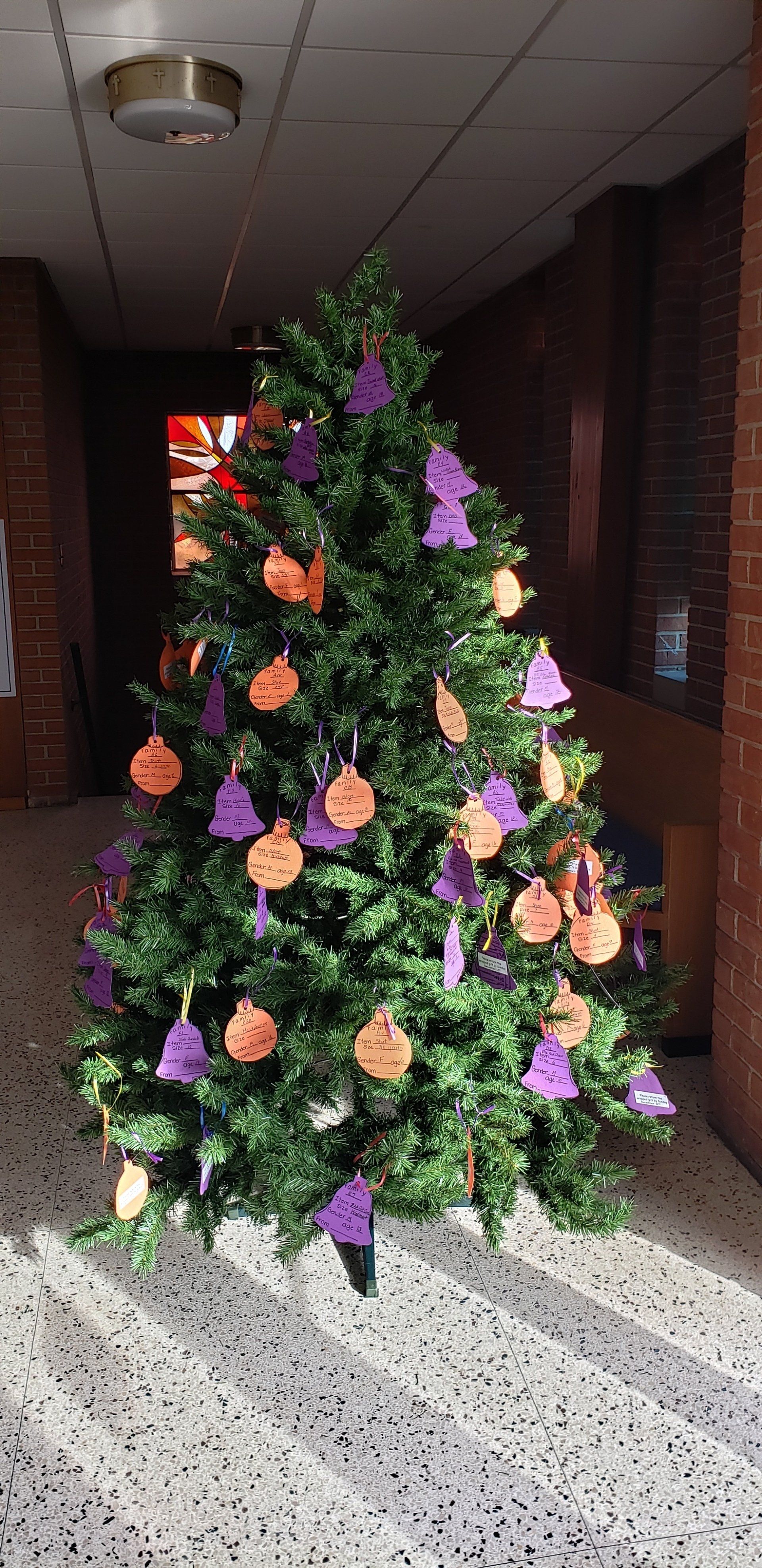 Decorated Christmas tree with purple, orange, and cream ornaments in a hallway