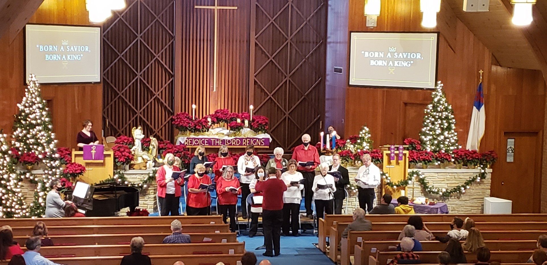 Choir and musicians performing in a church sanctuary decorated with Christmas trees and red poinsettias.