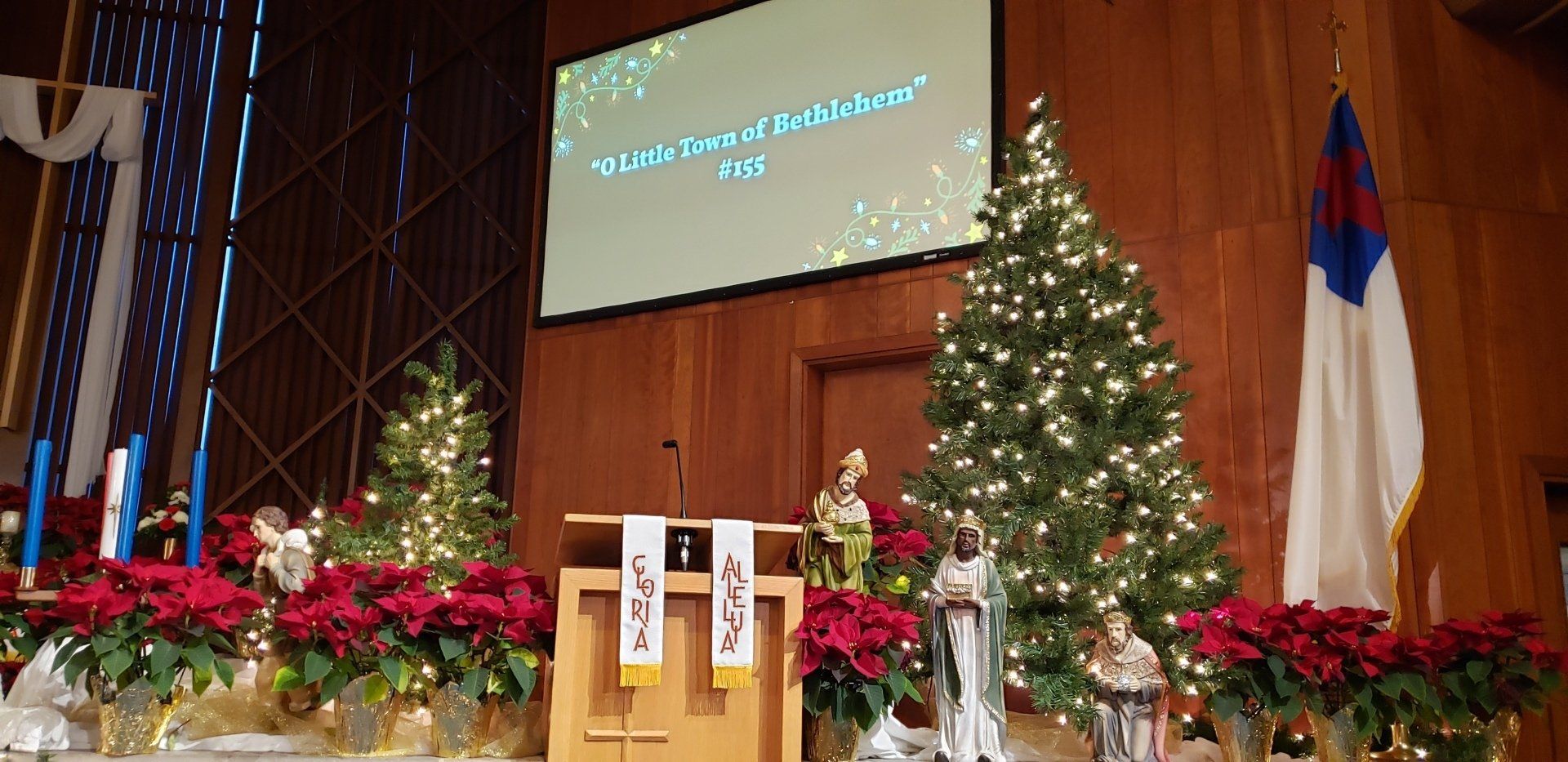 Church stage with podium, Christmas tree, poinsettias, and a projected presentation screen