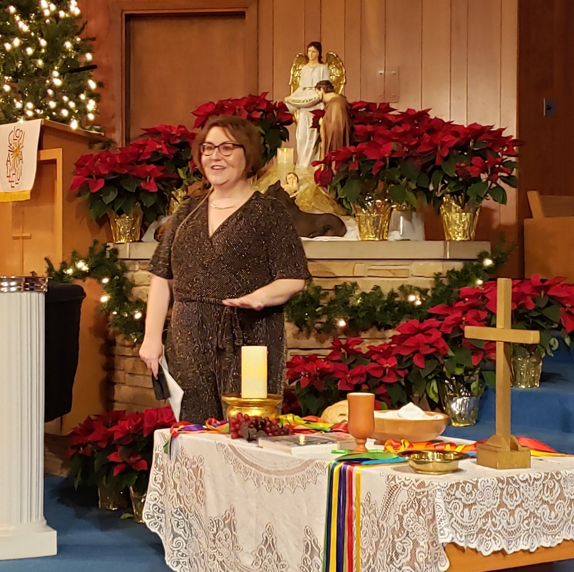 Woman standing in a church decorated with poinsettias beside a lit altar and Advent candles