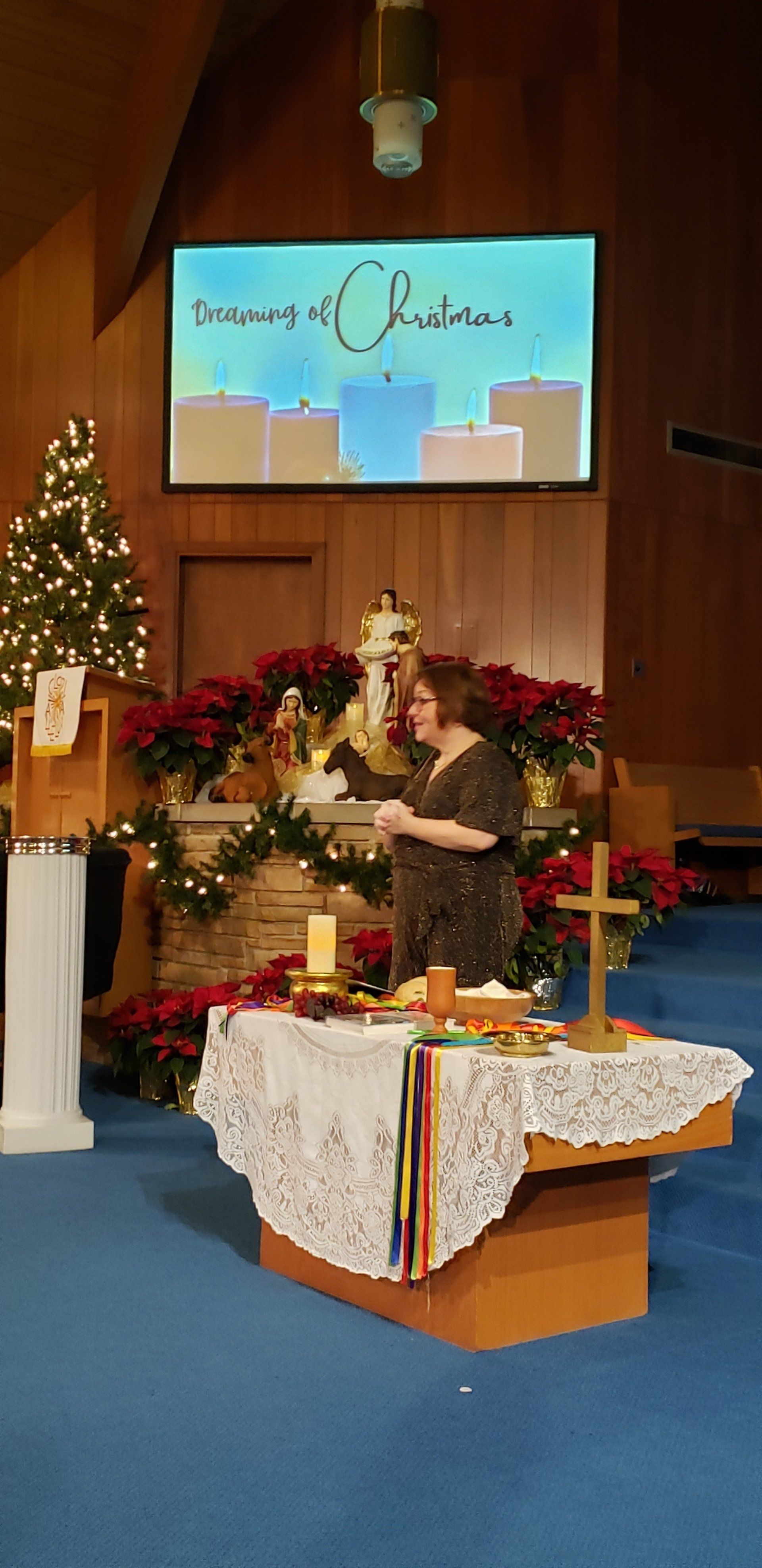 Church sanctuary with Christmas decorations, altar table, and floral arrangement before a screen