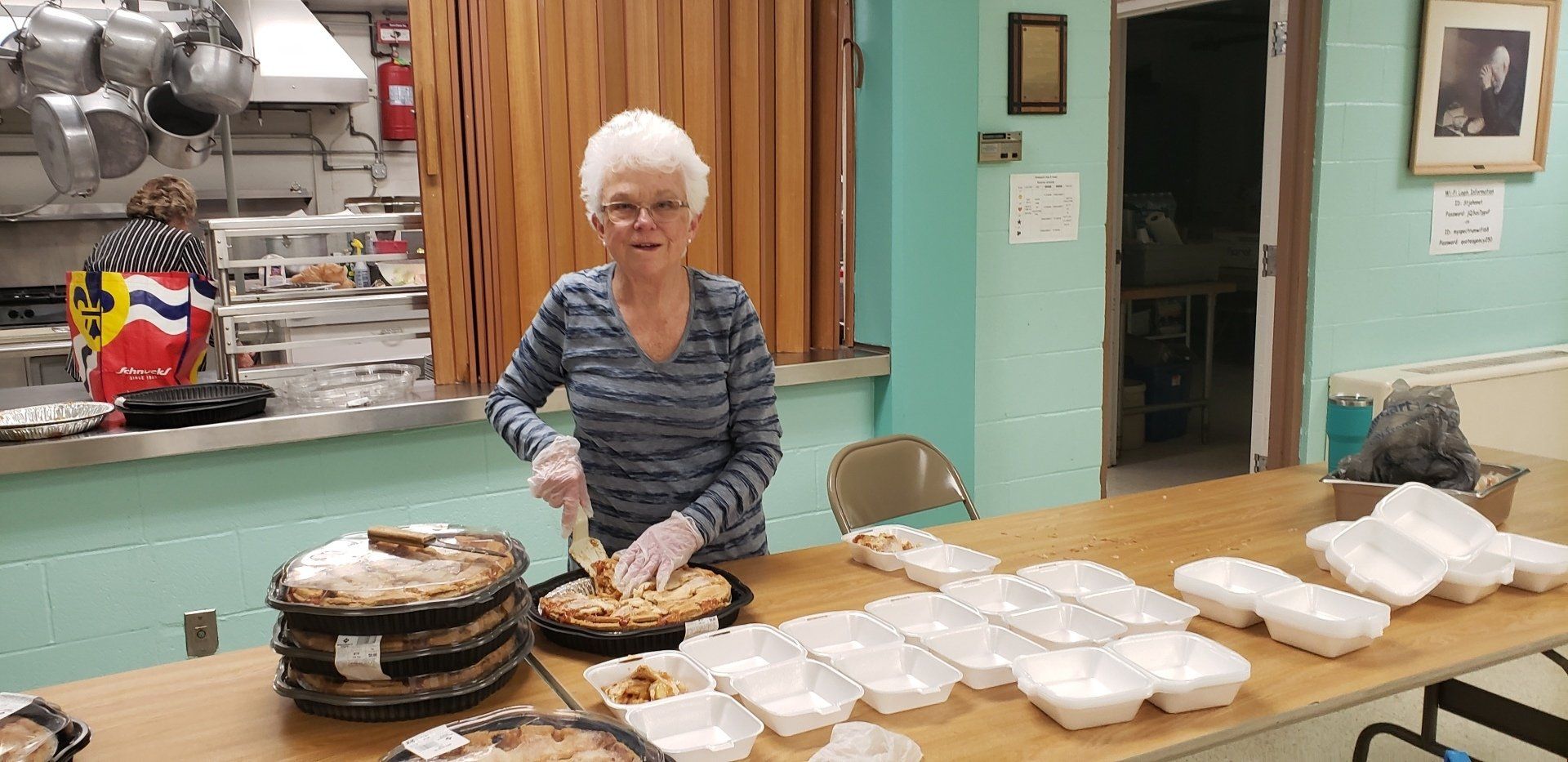Elderly woman arranging covered dishes on a table in a community kitchen