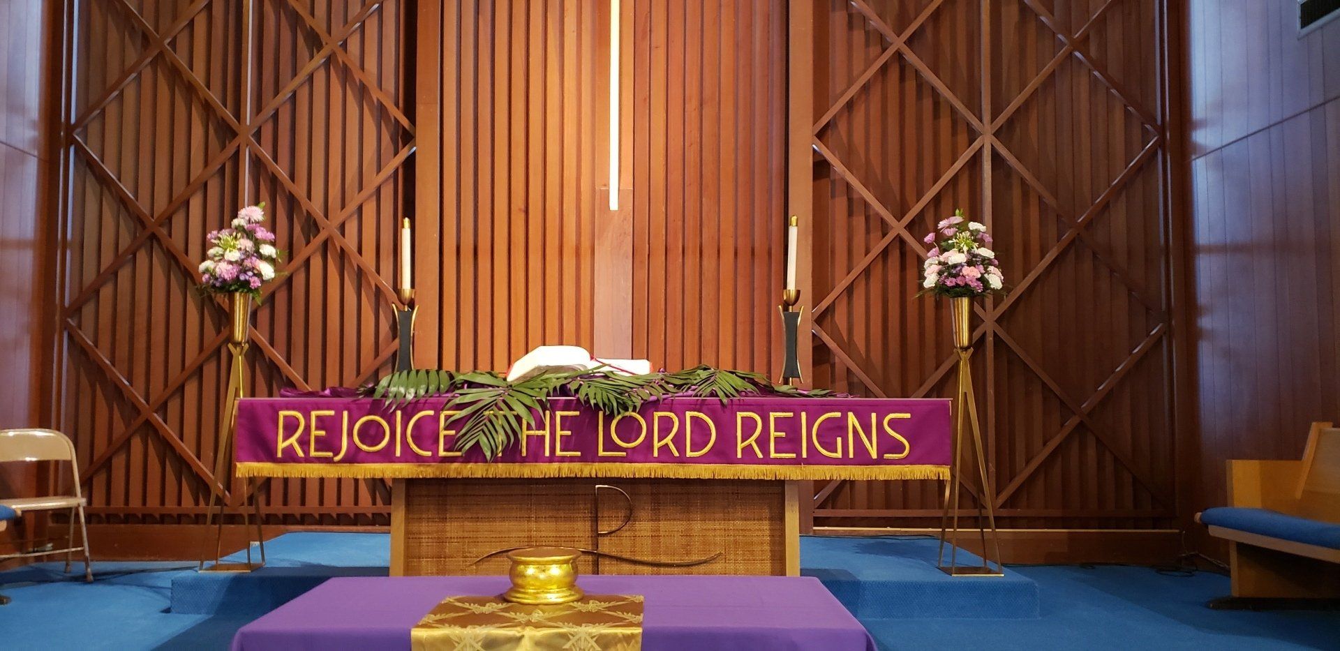 Church altar with purple drapery and flowers, reading “REJOICE, THE LORD REIGNS” above a central cross