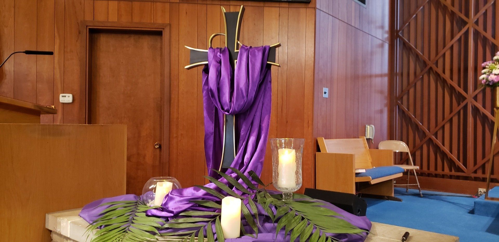Purple-draped altar with candles and flowers in a wood-paneled church sanctuary